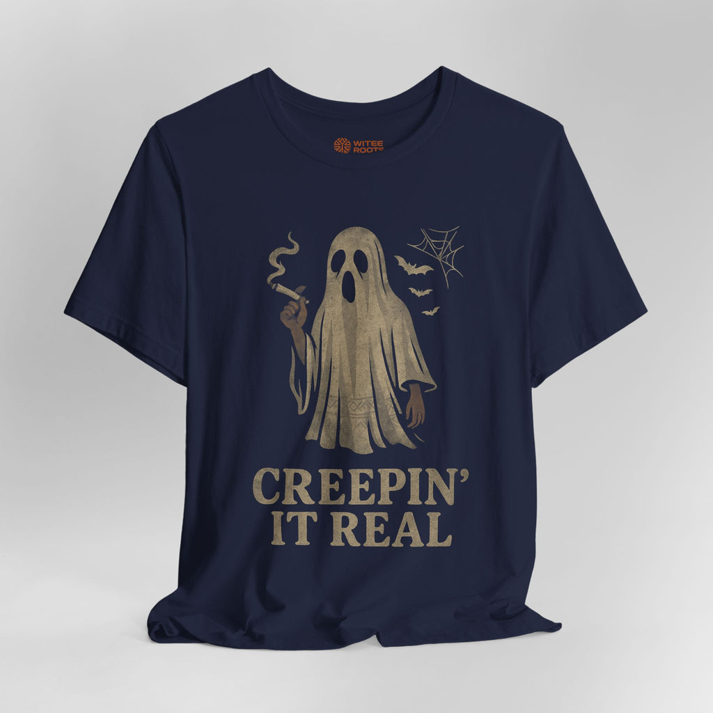 A navy blue short-sleeve t-shirt with a vintage-style beige graphic of a ghost holding a cigarette, accompanied by the text 'CREEPIN' IT REAL' and small spiderwebs and bats.