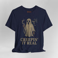 A navy blue short-sleeve t-shirt with a vintage-style beige graphic of a ghost holding a cigarette, accompanied by the text 'CREEPIN' IT REAL' and small spiderwebs and bats.