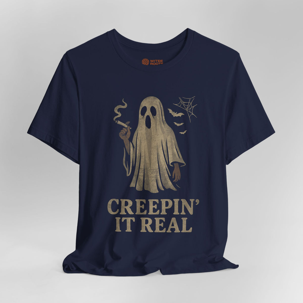 A navy blue short-sleeve t-shirt with a vintage-style beige graphic of a ghost holding a cigarette, accompanied by the text 'CREEPIN' IT REAL' and small spiderwebs and bats.