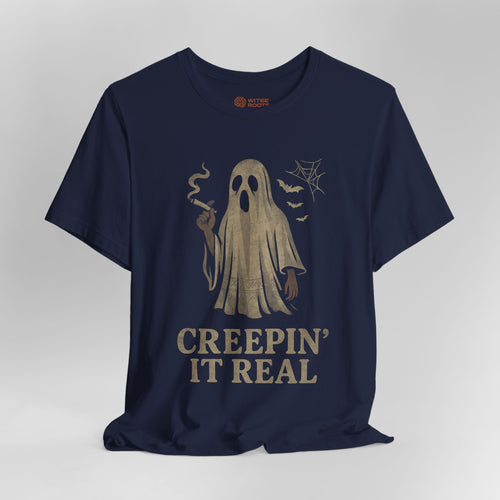 A navy blue short-sleeve t-shirt with a vintage-style beige graphic of a ghost holding a cigarette, accompanied by the text 'CREEPIN' IT REAL' and small spiderwebs and bats.
