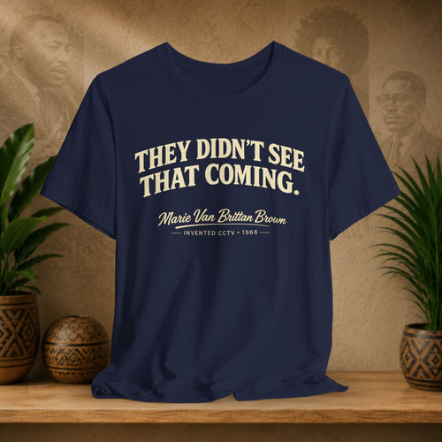 Navy blue t-shirt with white text on a wooden surface with plants and a vintage-style portrait in the background.