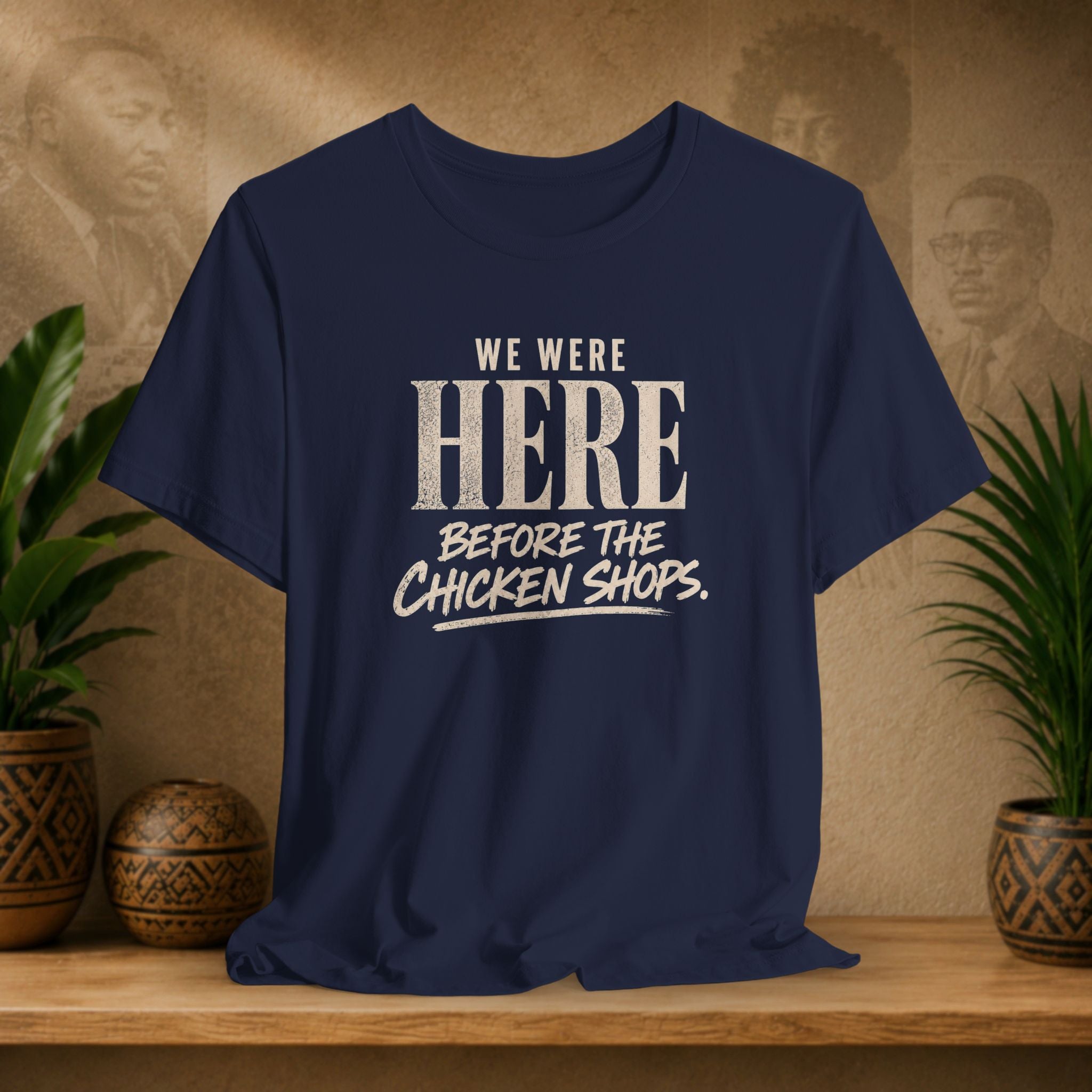 Navy blue t-shirt with white text on a wooden surface with plants and a textured wall background