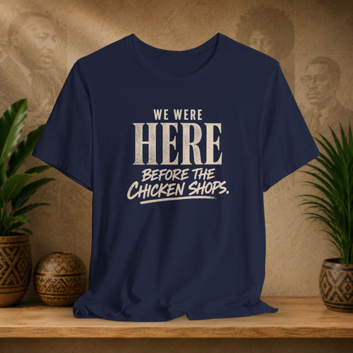 Navy blue t-shirt with white text on a wooden surface with plants and a textured wall background