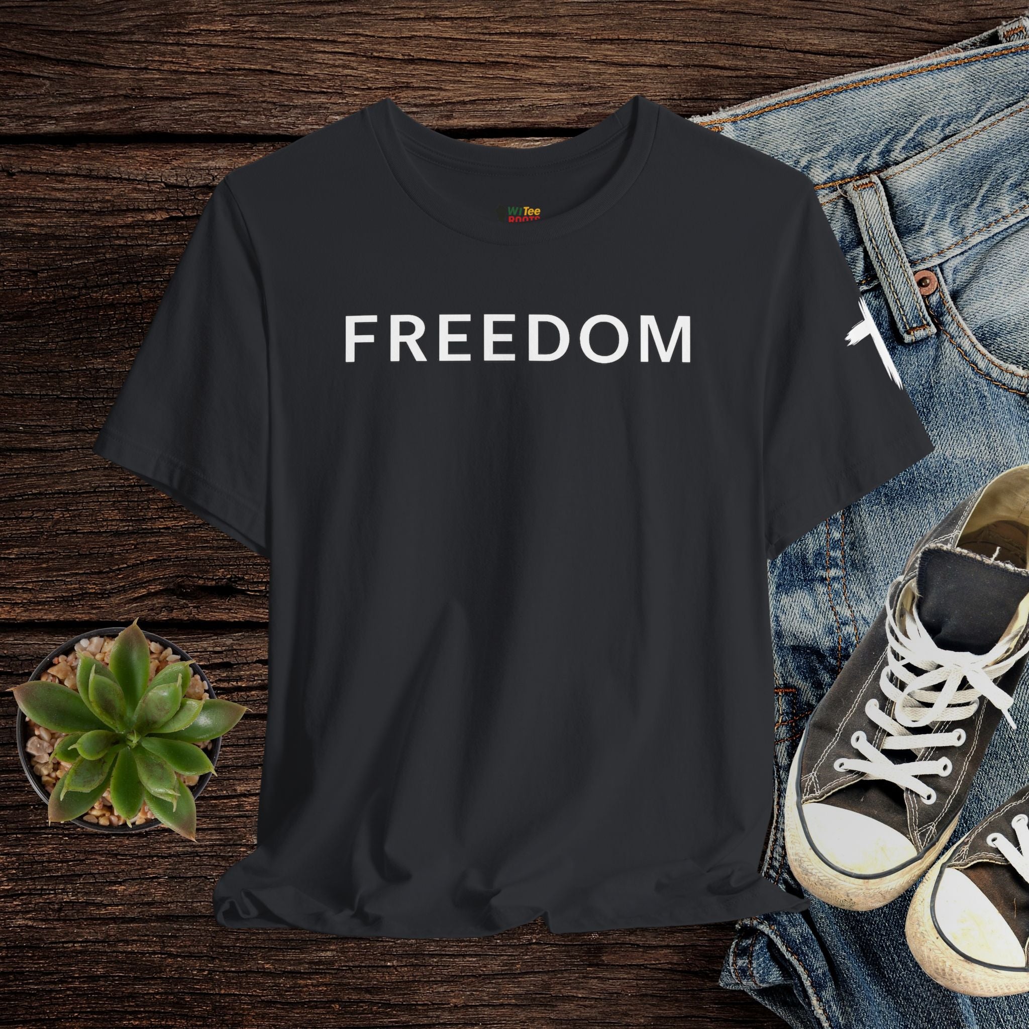 Black t-shirt with 'FREEDOM' text on a wooden surface with jeans and sneakers.