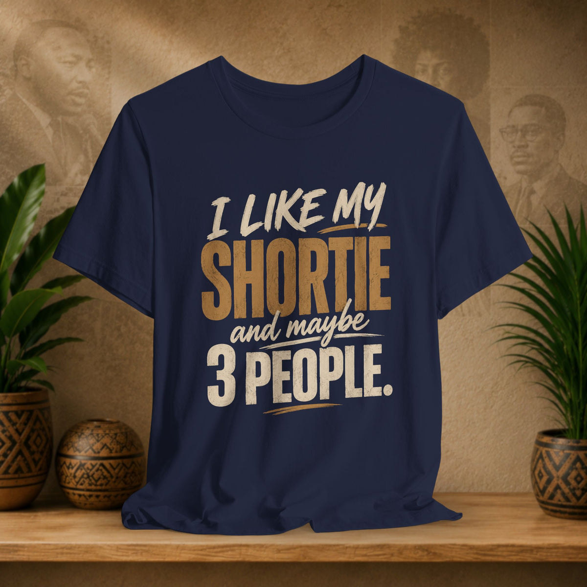 A navy graphic t-shirt displayed on a wooden shelf. The shirt features a humorous slogan printed in white and tan lettering: 'I LIKE MY SHORTIE and maybe 3 PEOPLE.