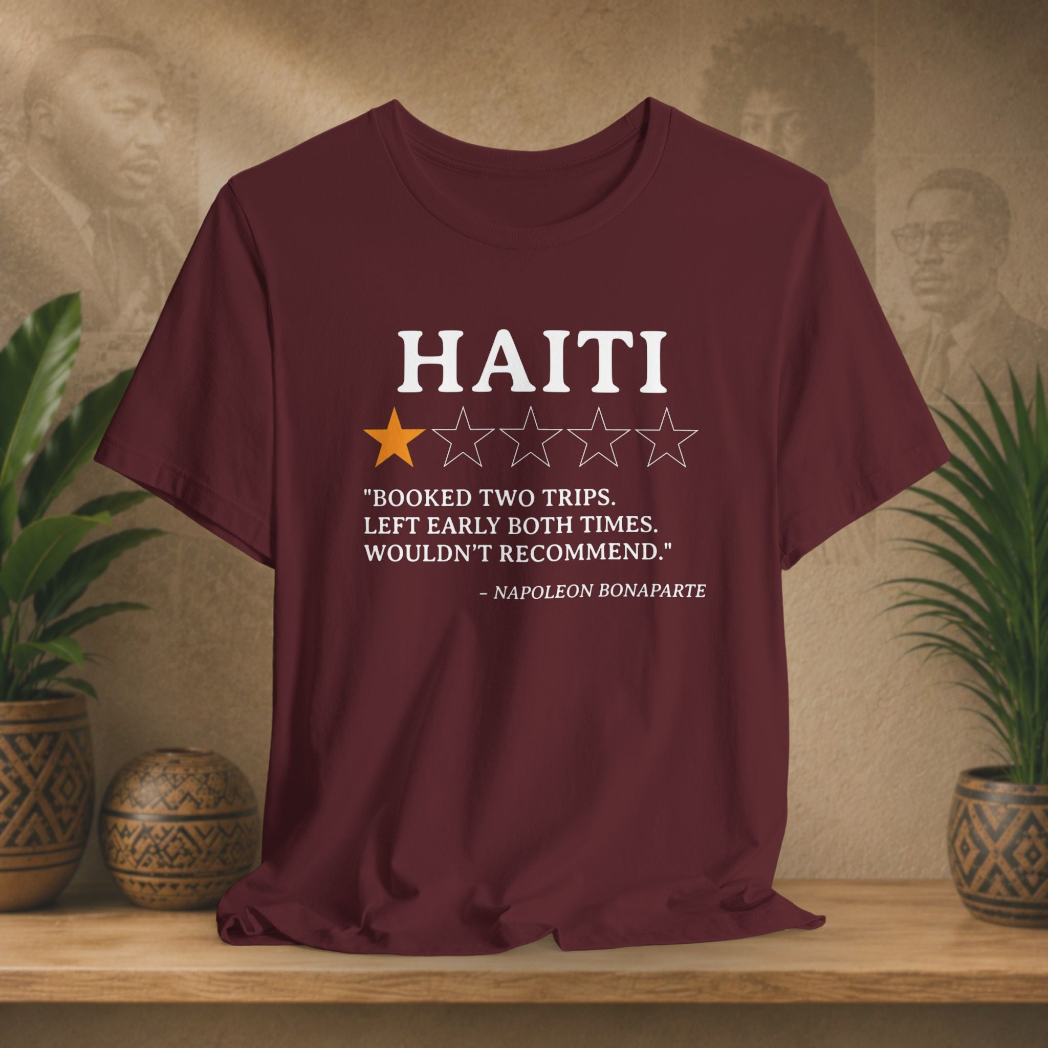 Maroon t-shirt with Haiti-themed text and stars on a wooden surface with plants and decorative items.
