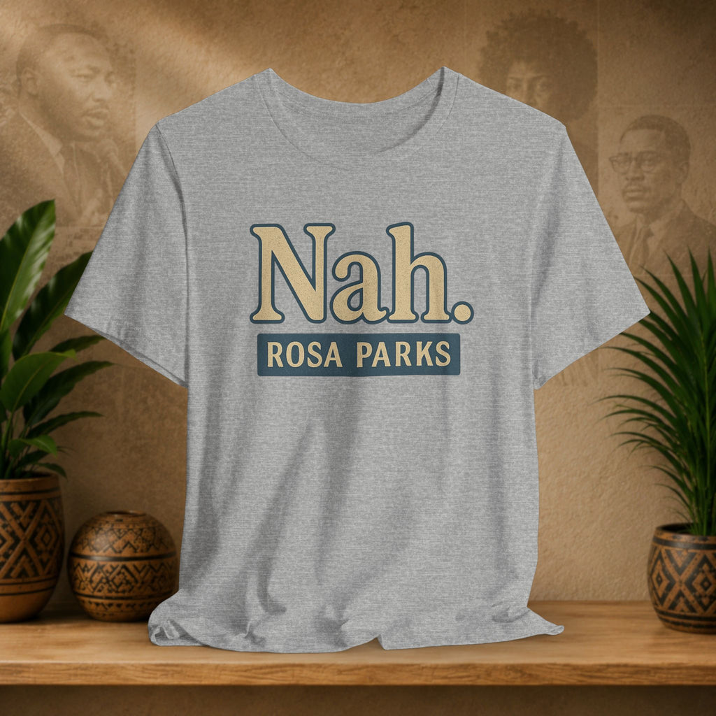 Gray t-shirt with 'Nah. Rosa Parks' text on a wooden shelf with plants and a blurred background.