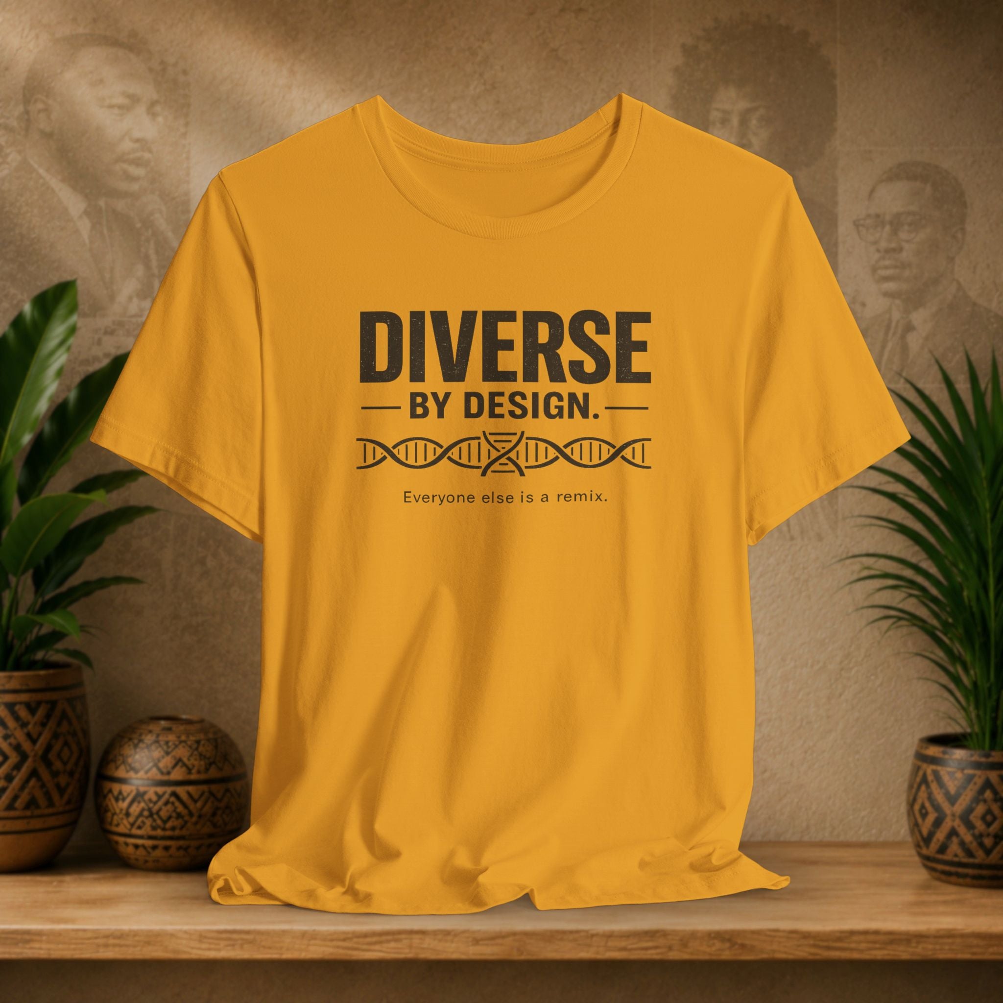 Yellow t-shirt with 'Diverse by Design' text on a wooden surface with plants and a textured wall background.