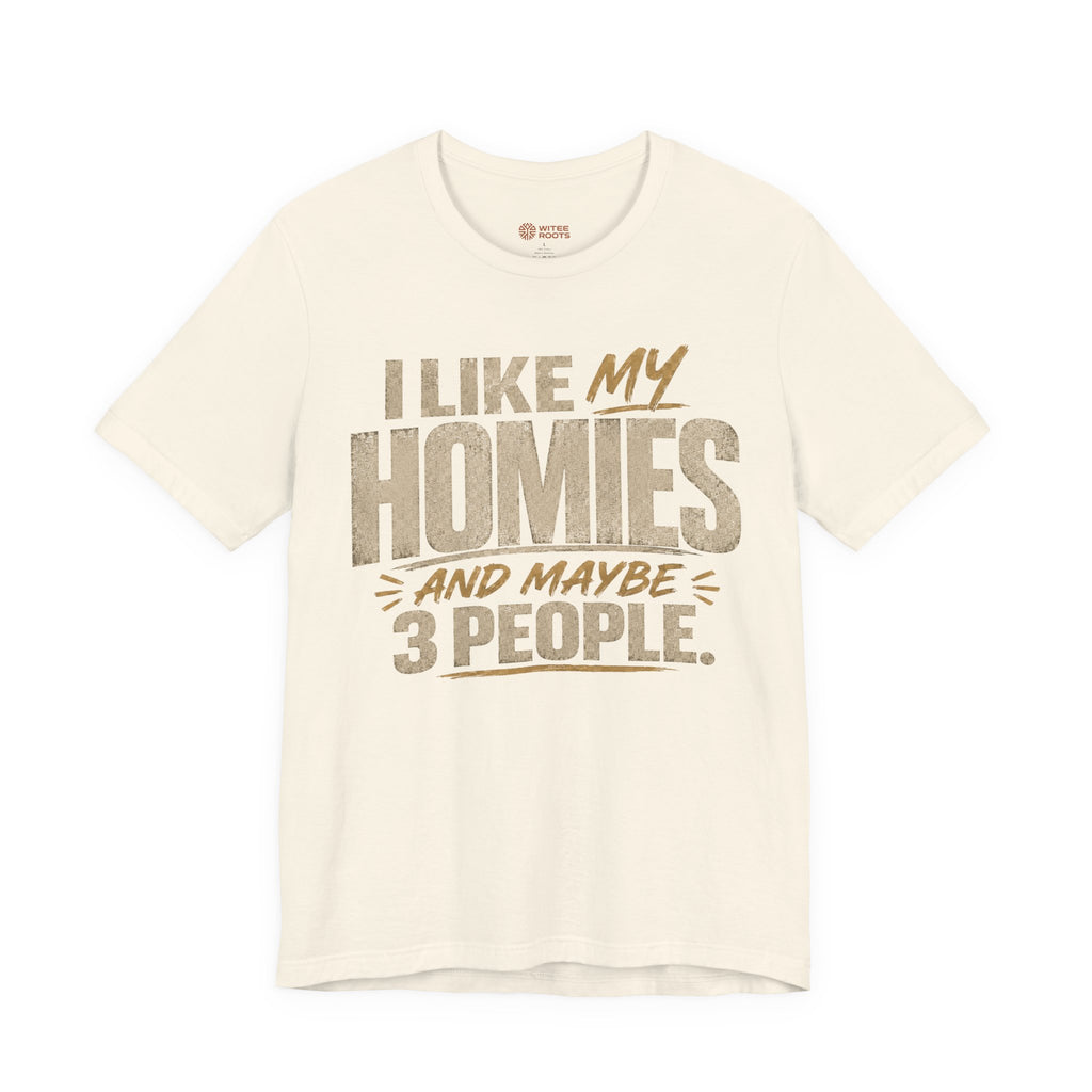 A beige graphic t-shirt displayed on a white background. The shirt features a humorous slogan printed in white and tan lettering: 'I LIKE MY HOMIES and maybe 3 PEOPLE.