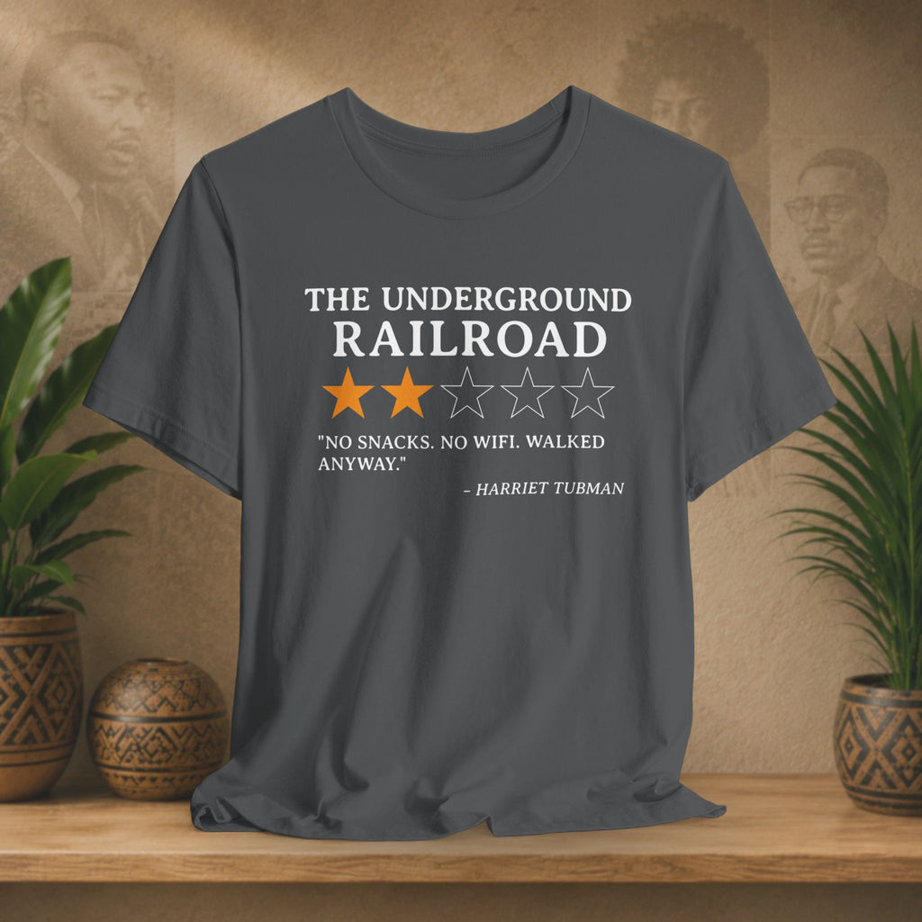Gray t-shirt with text and star ratings on a wooden surface with plants and a textured wall background