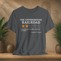 Gray t-shirt with text and star ratings on a wooden surface with plants and a textured wall background