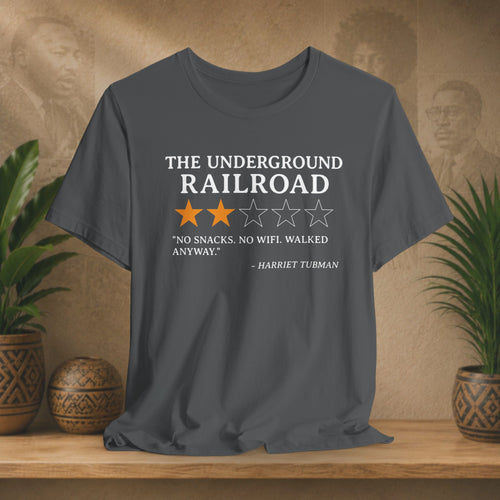 Gray t-shirt with text and star ratings on a wooden surface with plants and a textured wall background