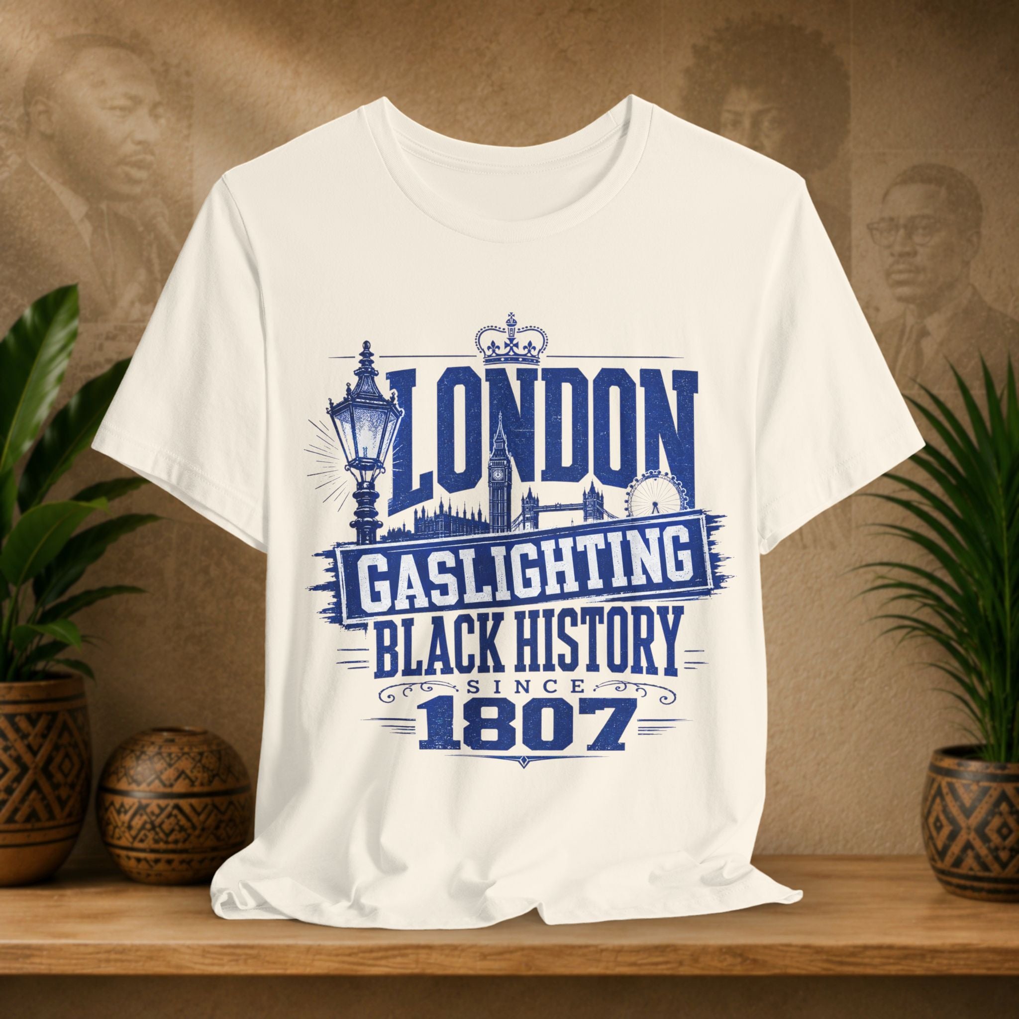 Beige t-shirt with 'London Gaslighting Black History Since 1807' design on a wooden surface with plants and a blurred background.