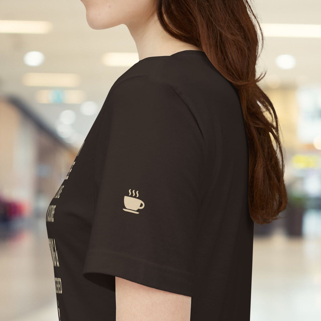 Person wearing a black t-shirt with a coffee cup logo in a blurred indoor setting