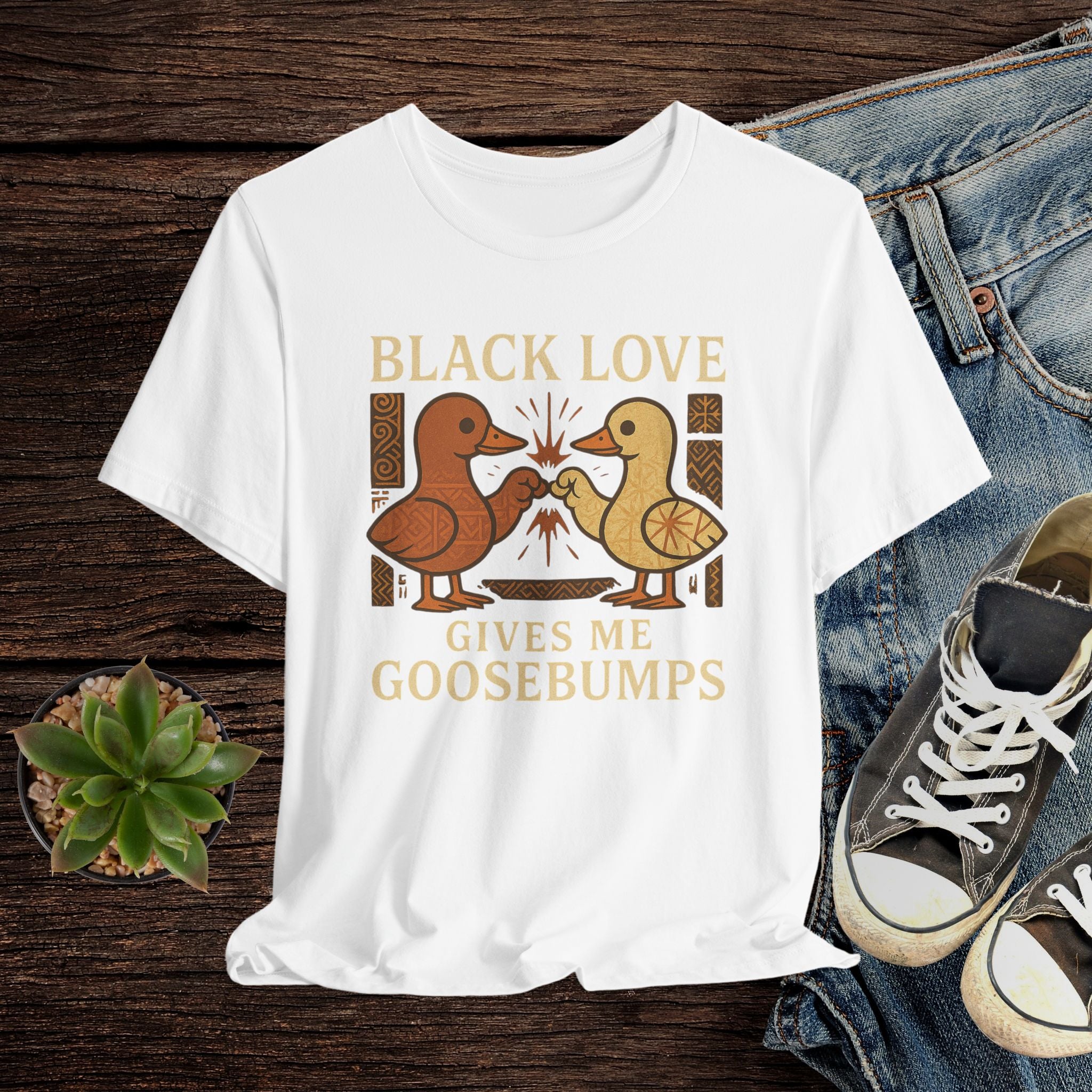 White t-shirt with 'Black Love Gives Me Goosebumps' graphic on a wooden surface with jeans and sneakers.