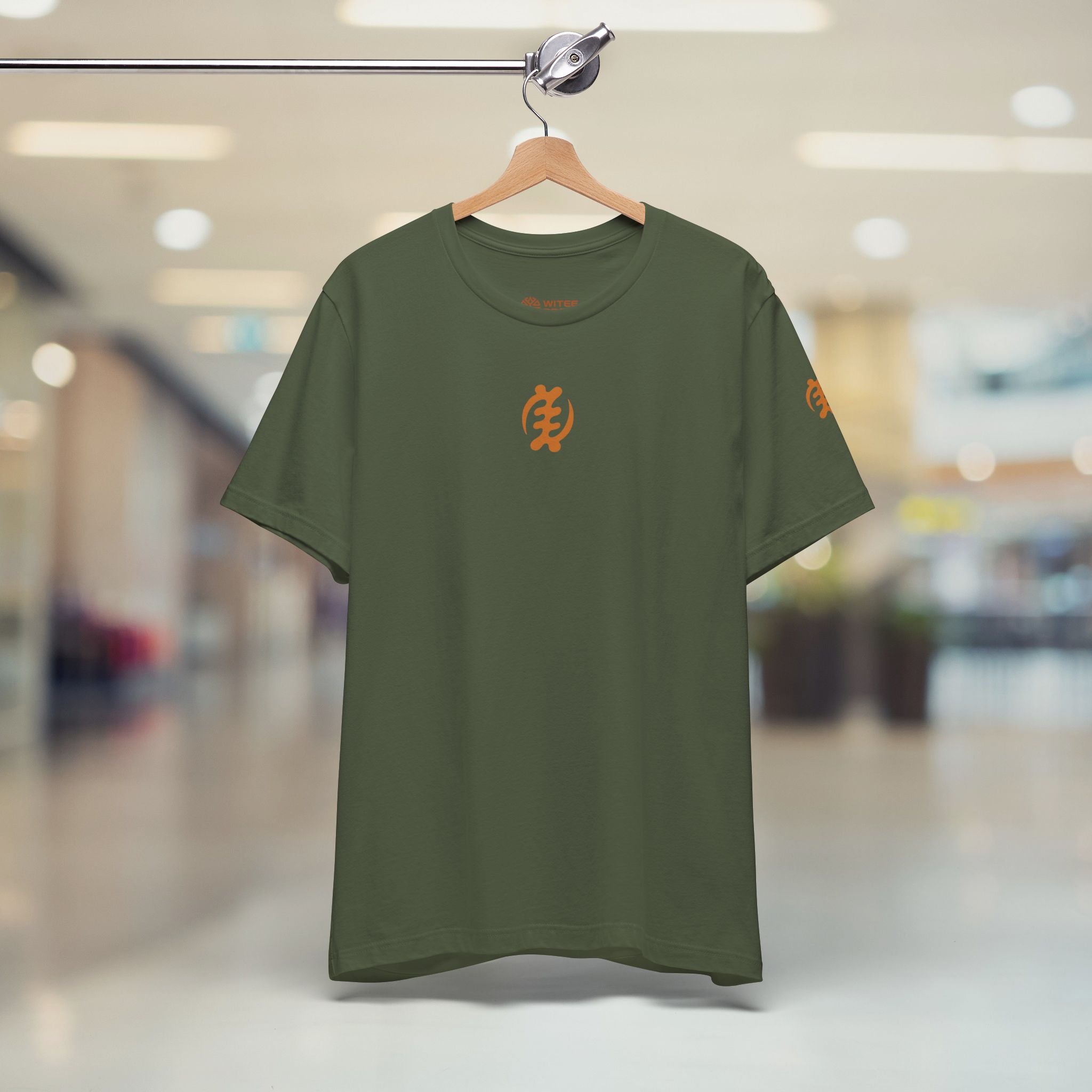 Green t-shirt with orange logo on a hanger against a blurred indoor background