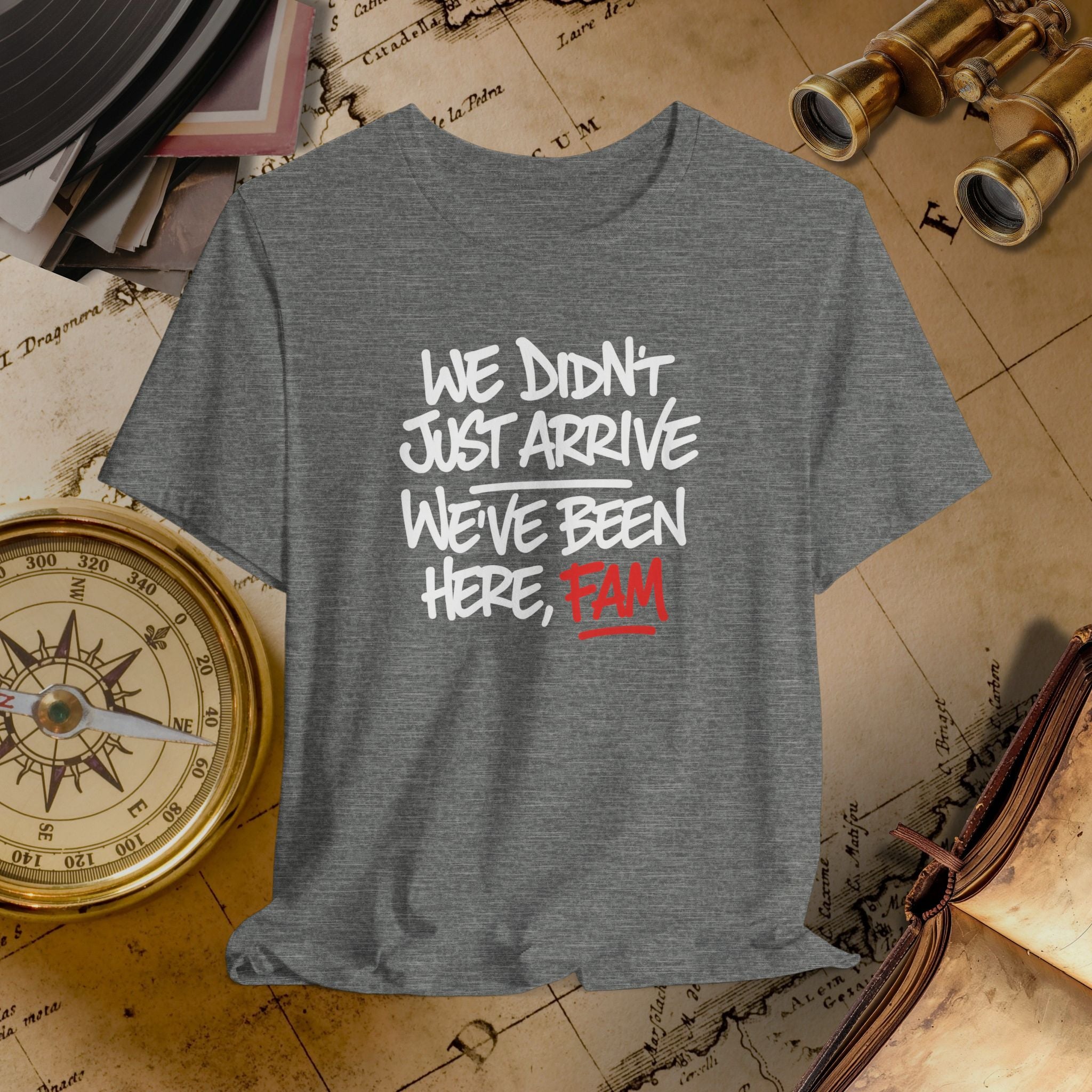 Gray t-shirt with text 'WE DIDN'T JUST ARRIVE WE'VE BEEN HERE, FAM' on a vintage map background