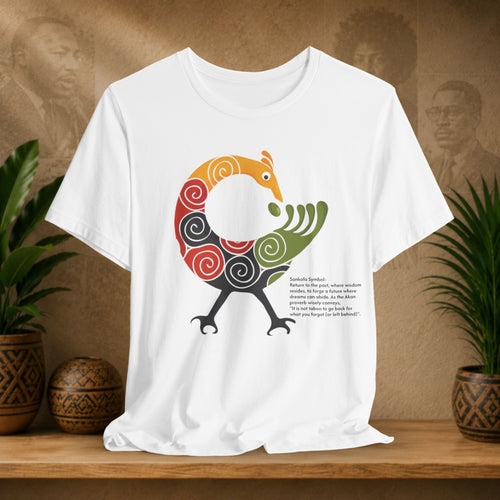 White t-shirt with a colorful bird design on a wooden surface with plants and a textured wall in the background