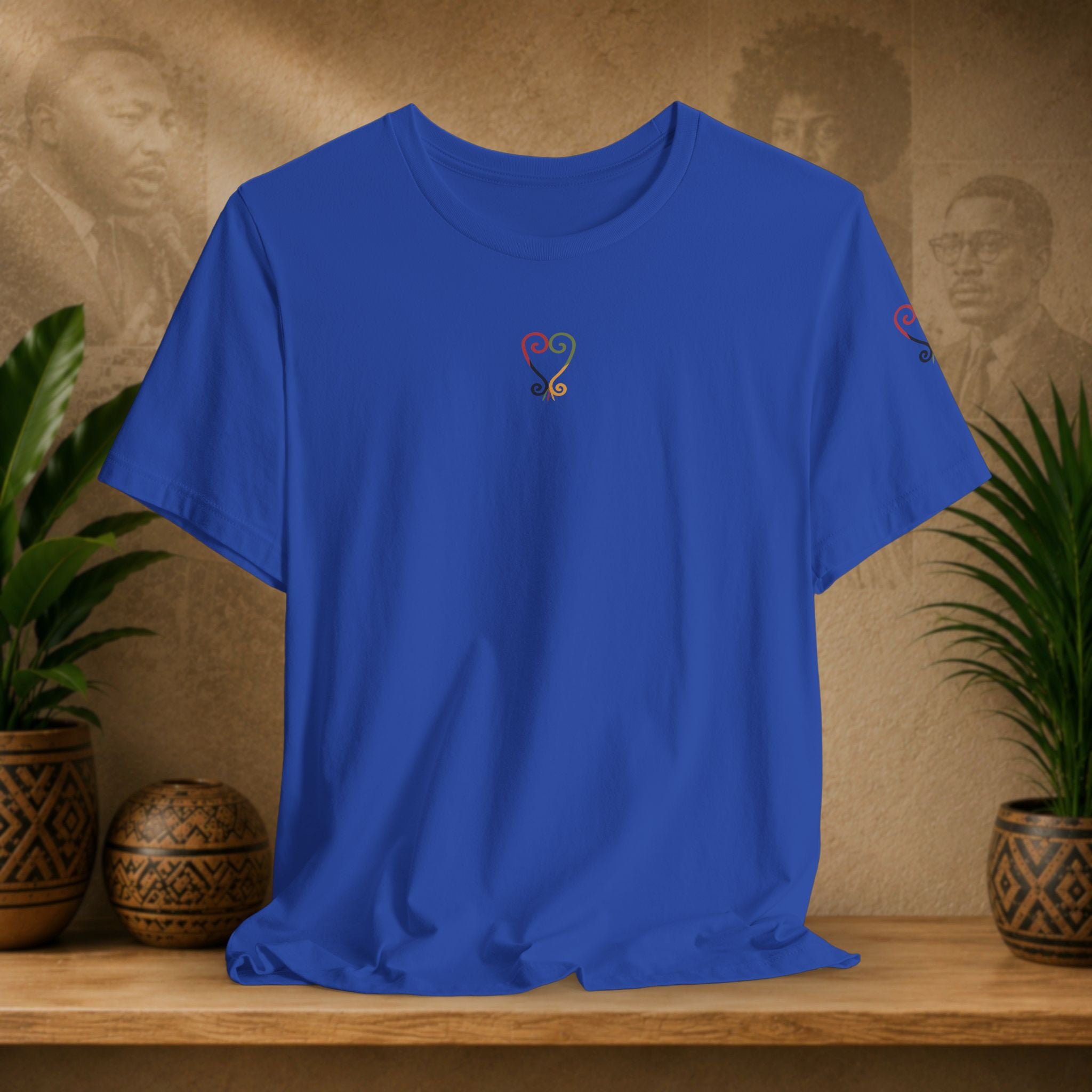 Blue t-shirt with a colorful logo on a wooden surface with plants and a textured wall background