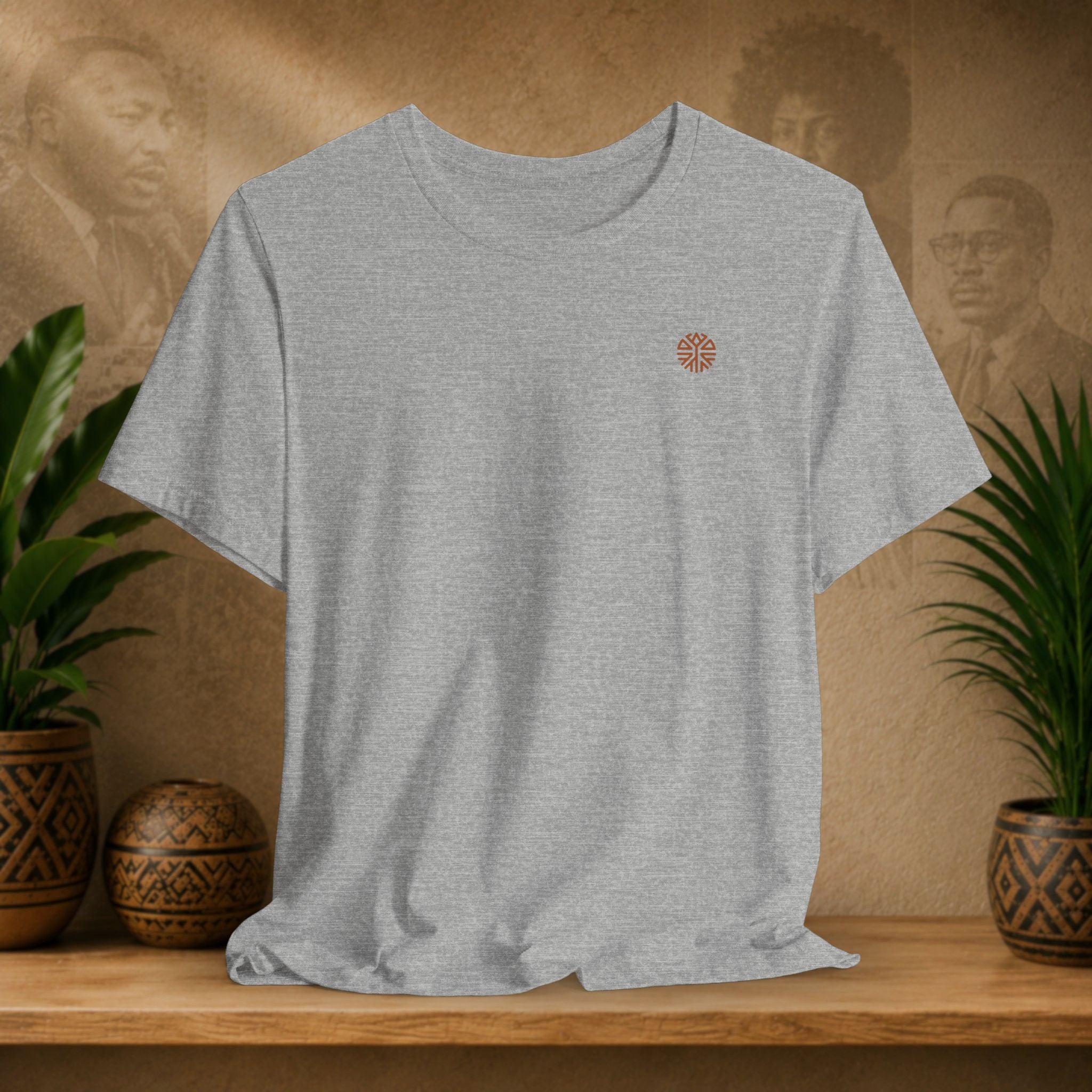 Gray t-shirt with a small logo on a wooden shelf with plants and a textured wall background