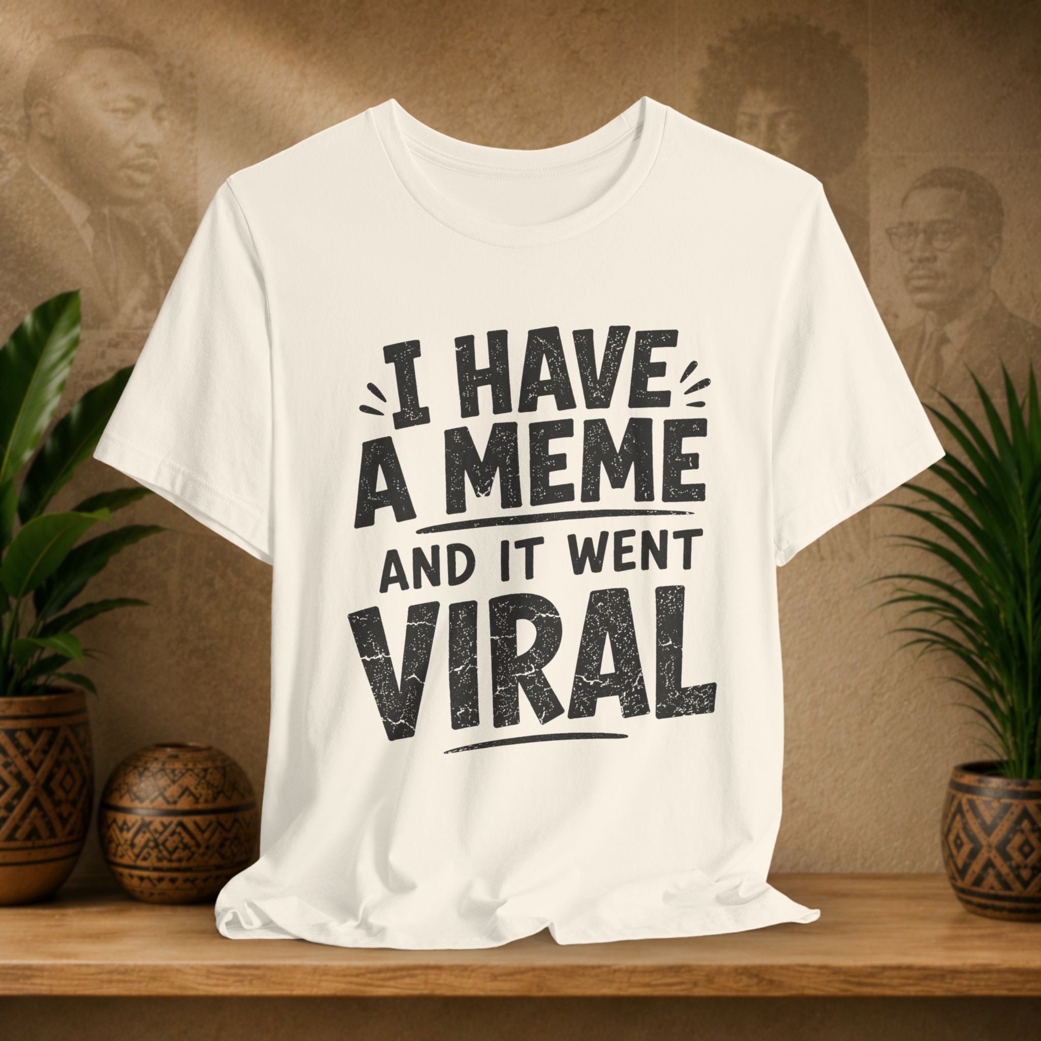Beige t-shirt with 'I have a meme and it went viral' text on a wooden surface with plants and a textured wall background.