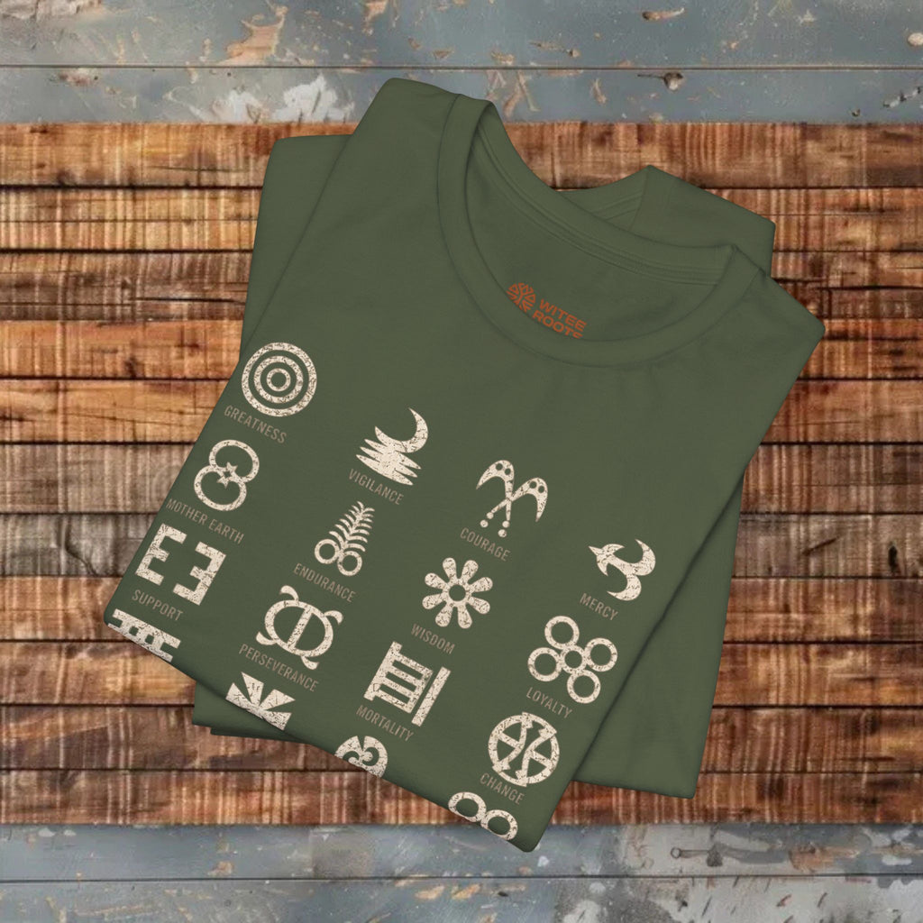 An olive green folded t-shirt with a graphic print of various tribal symbols and words, displayed on a rustic wooden plank background.