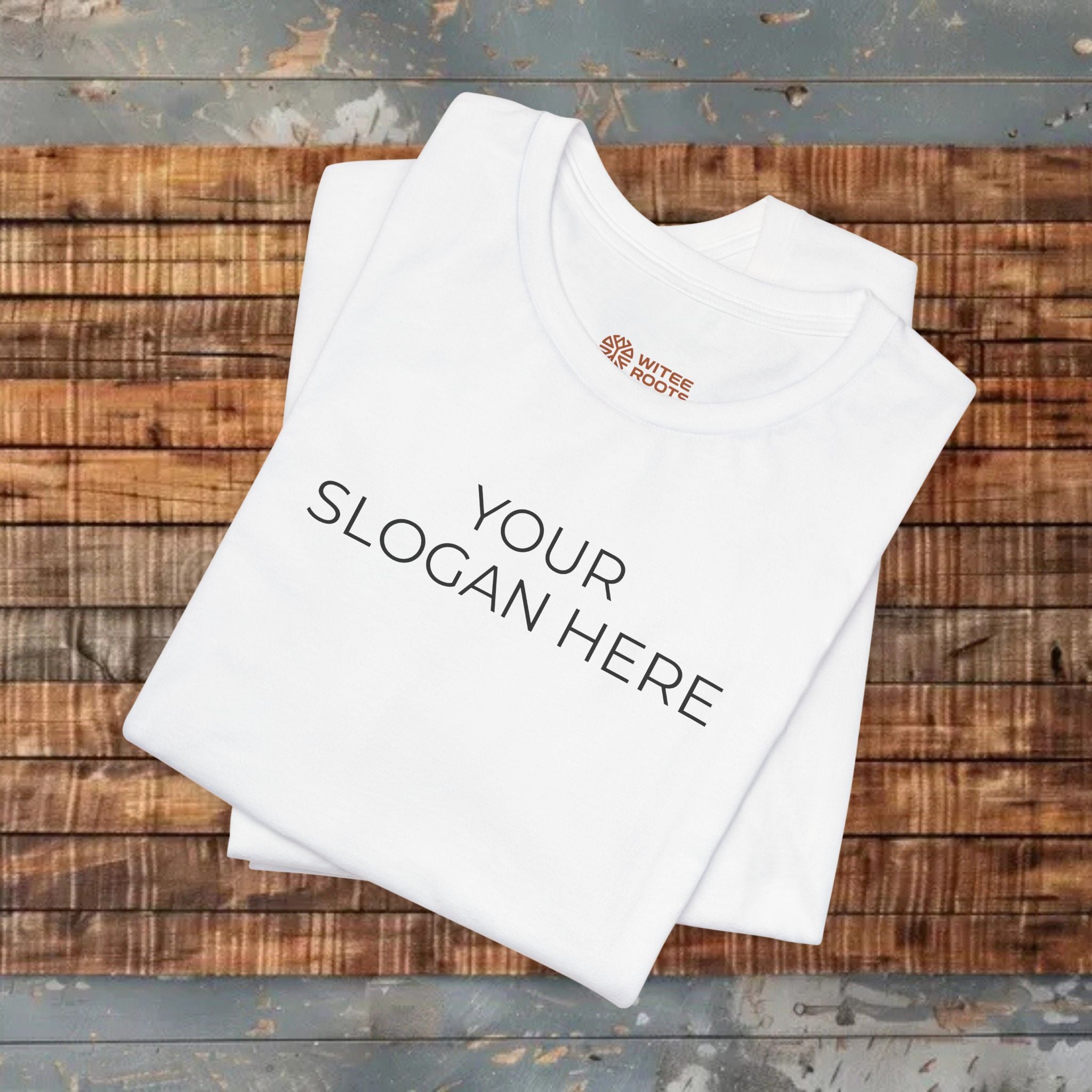 A folded white t-shirt with the text 'Print it your way' printed in black on the front, displayed on a rustic wooden plank surface.