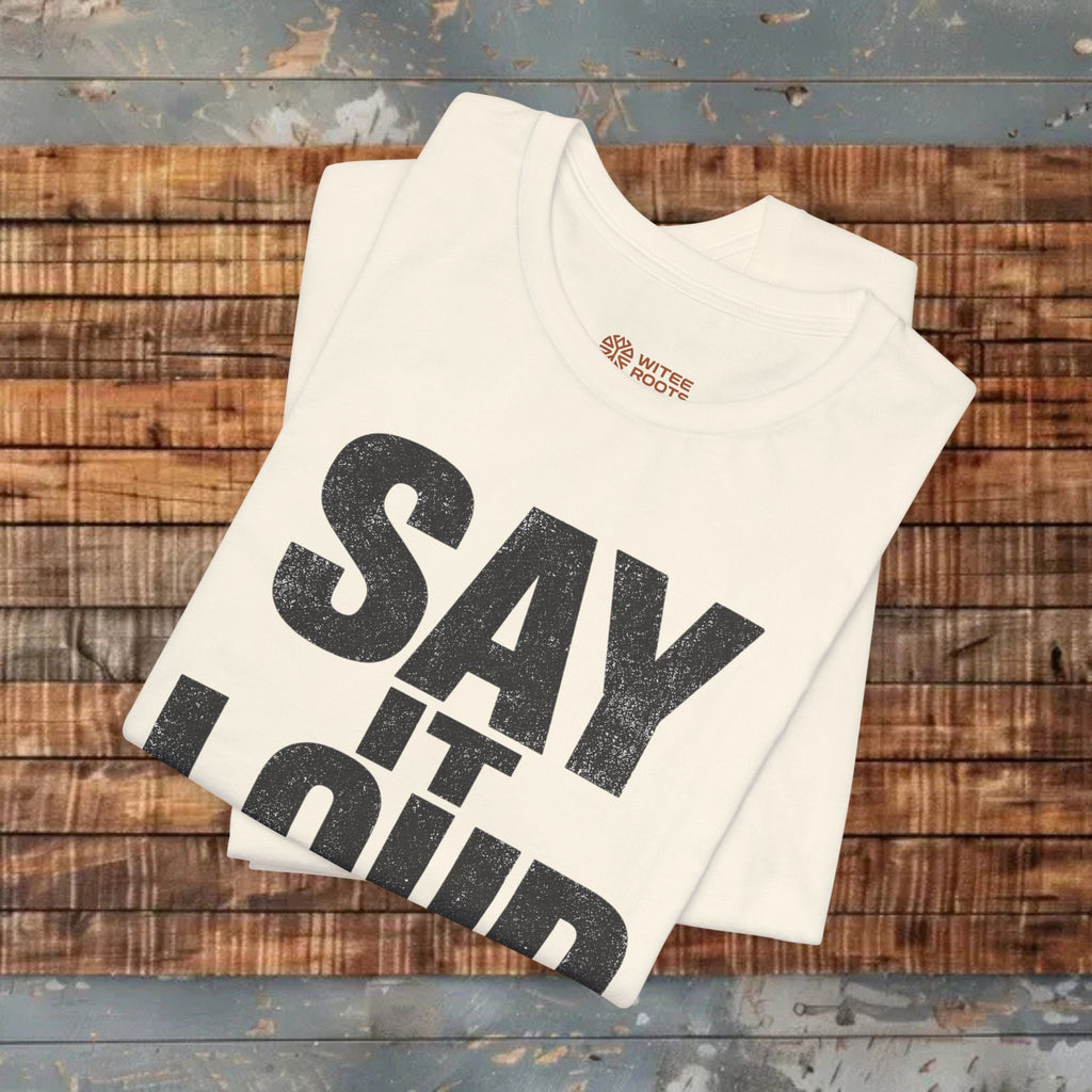 Stack of t-shirts with 'SAY IT OUT' text on a wooden surface