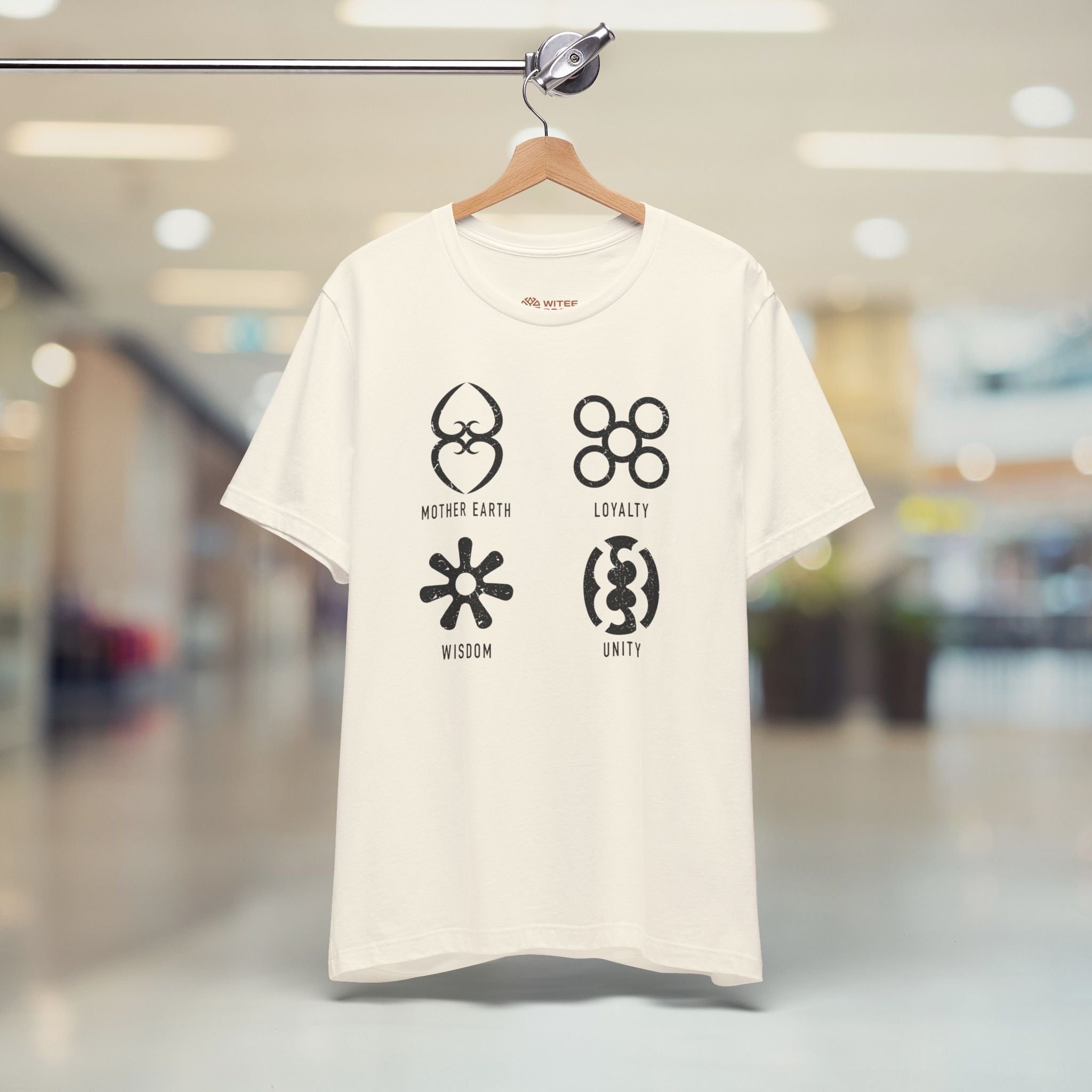 Sand t-shirt with black symbols and text on a hanger in a blurred indoor setting