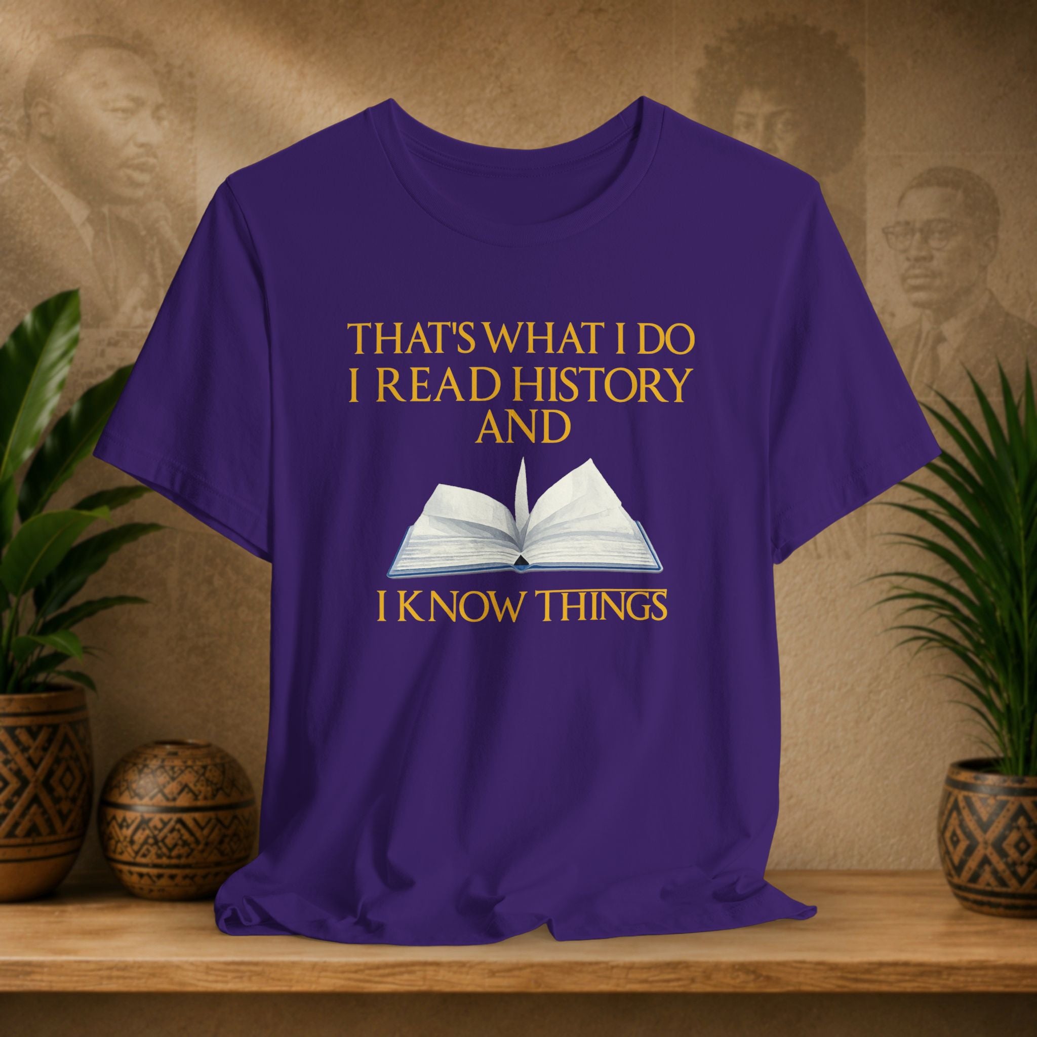 Purple t-shirt with text and book graphic on a wooden surface with plants and decorative items.