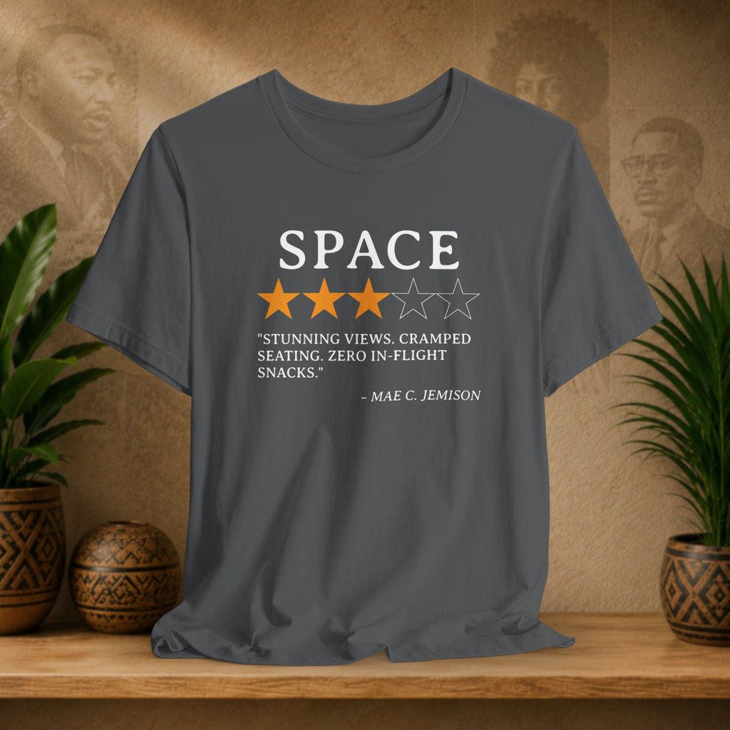 Gray t-shirt with space-themed graphic and text on a wooden surface with plants and decorative items.