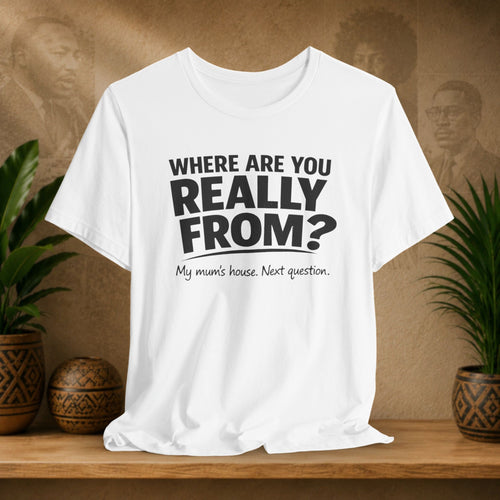 White t-shirt with humorous text design on a wooden surface with plants and a textured wall background