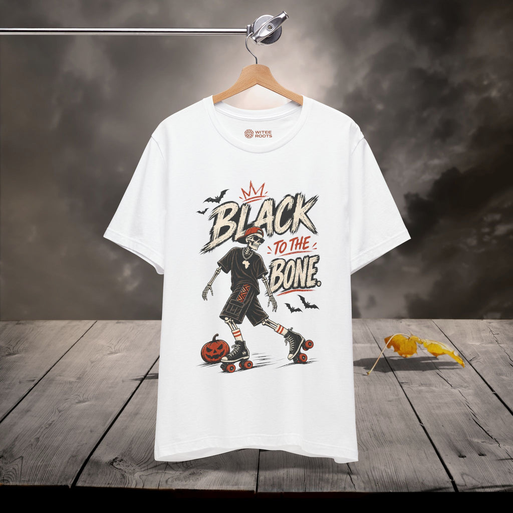 A white graphic t-shirt hanging on a wooden hanger against a dark, smoky background with a wooden plank floor. The shirt features a Halloween-themed graphic with the text 'BLACK TO THE BONE' and an illustration of a skeleton roller skate.
