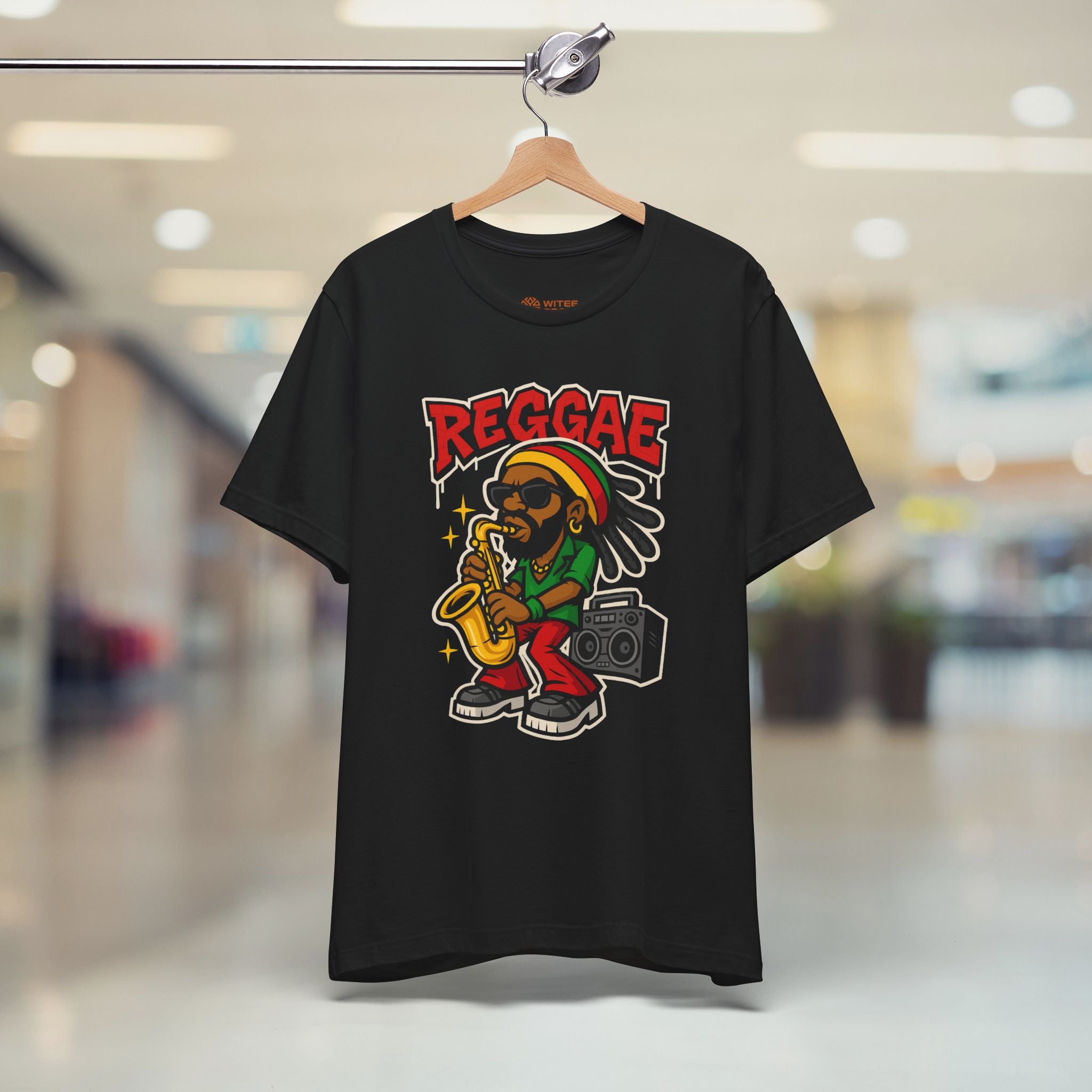 Black t-shirt with reggae-themed design featuring a person playing a saxophone and a radio, on a hanger with a blurred indoor background.