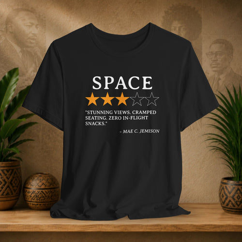 Black t-shirt with space-themed design on a wooden surface with plants and a decorative wall.