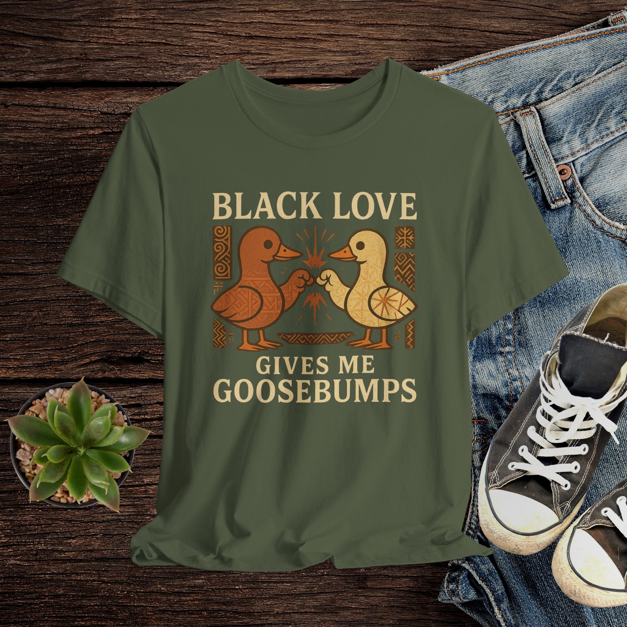 Green t-shirt with 'Black Love Gives Me Goosebumps' graphic on a wooden surface with jeans and sneakers.