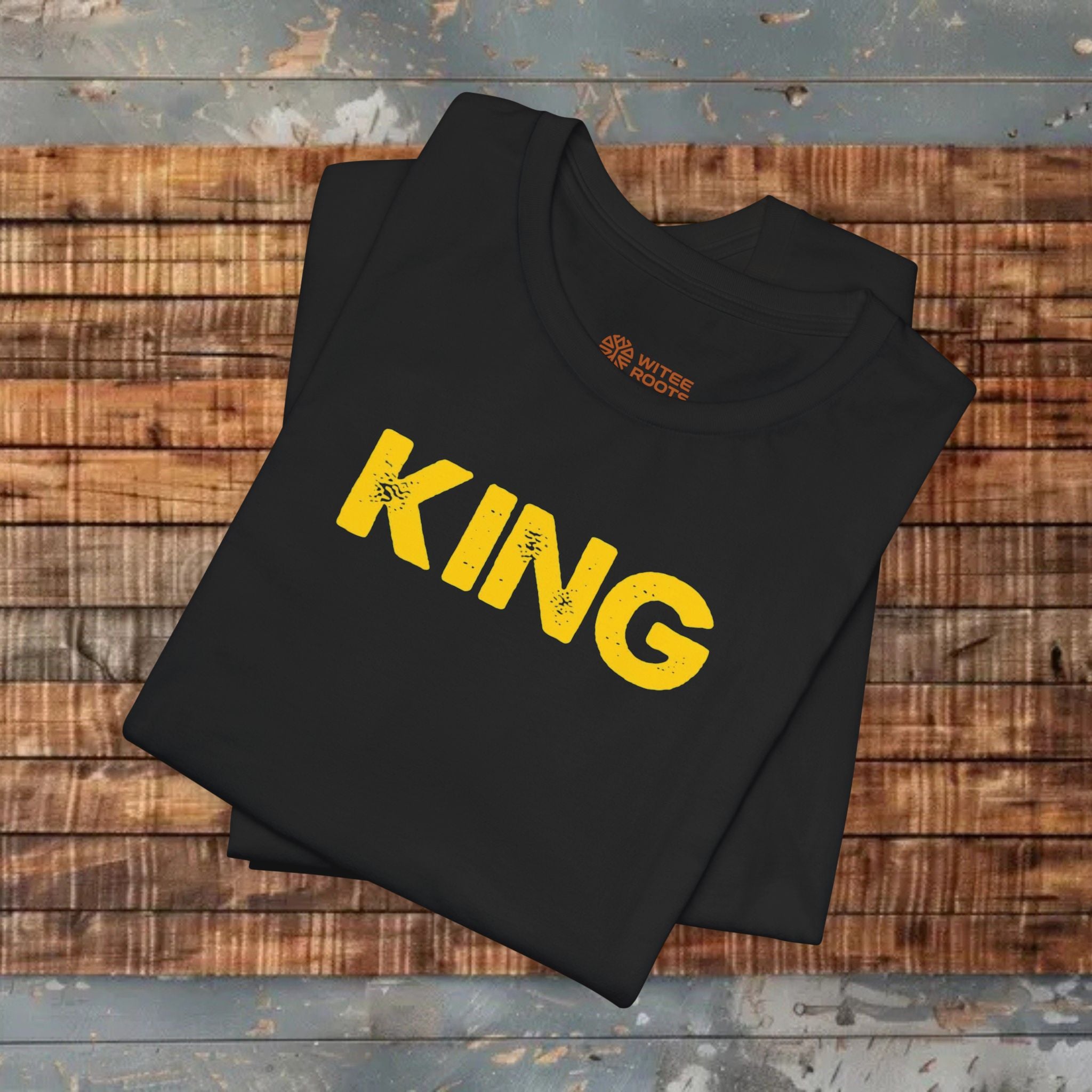 Black t-shirt with 'KING' in yellow on a wooden surface
