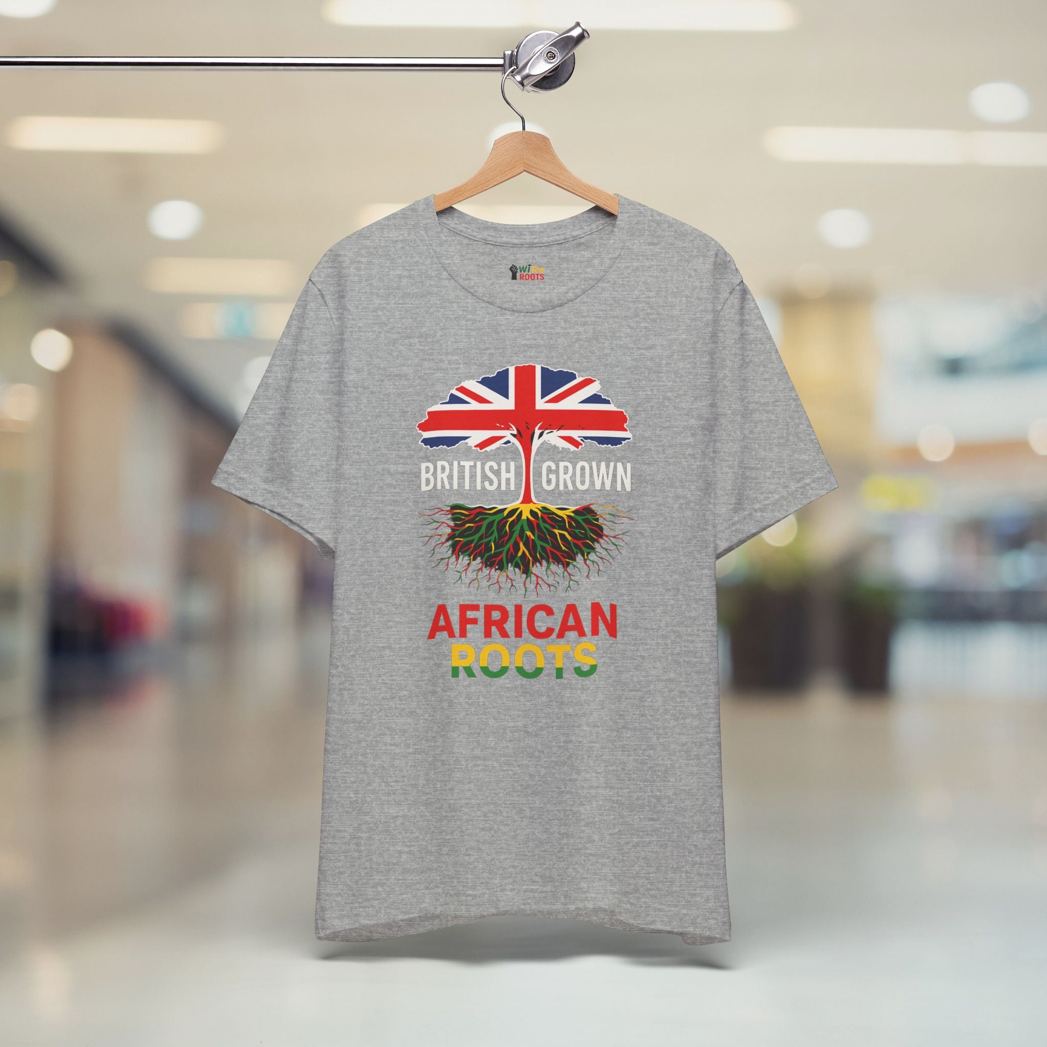 Gray t-shirt with a design of British flag and roots, text 'BRITISH GROWN AFRICAN ROOTS' on a hanger.