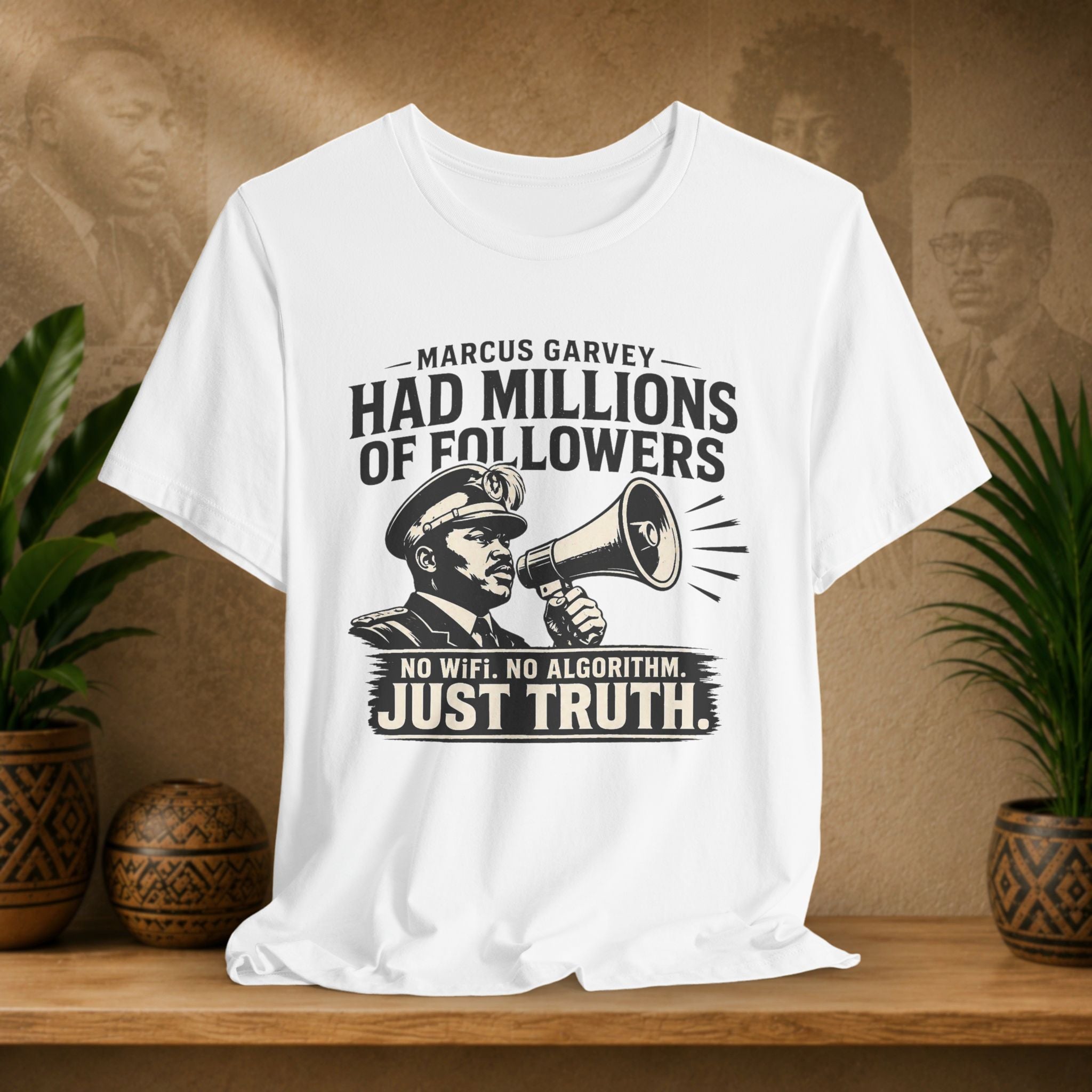 White t-shirt with a graphic and text on a wooden surface with plants and a textured wall in the background