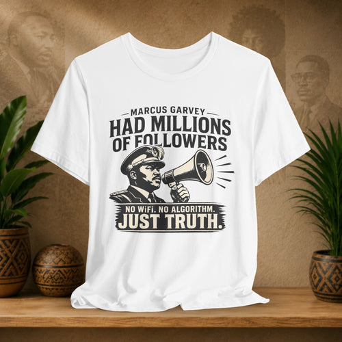 White t-shirt with a graphic and text on a wooden surface with plants and a textured wall in the background