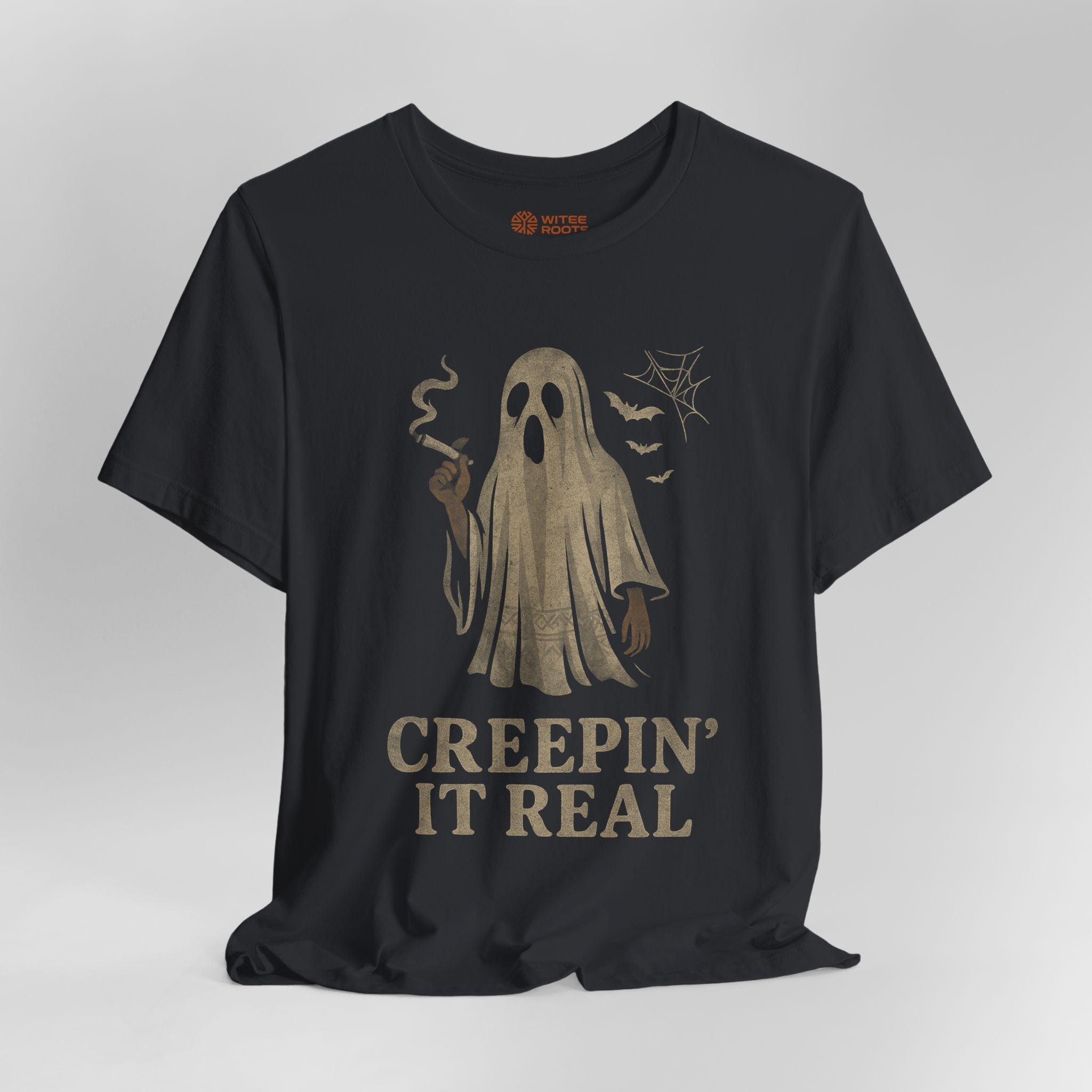A black short-sleeve t-shirt with a distressed beige graphic of a smoking ghost and the text 'CREEPIN' IT REAL' on the front, displayed against a neutral gray background.