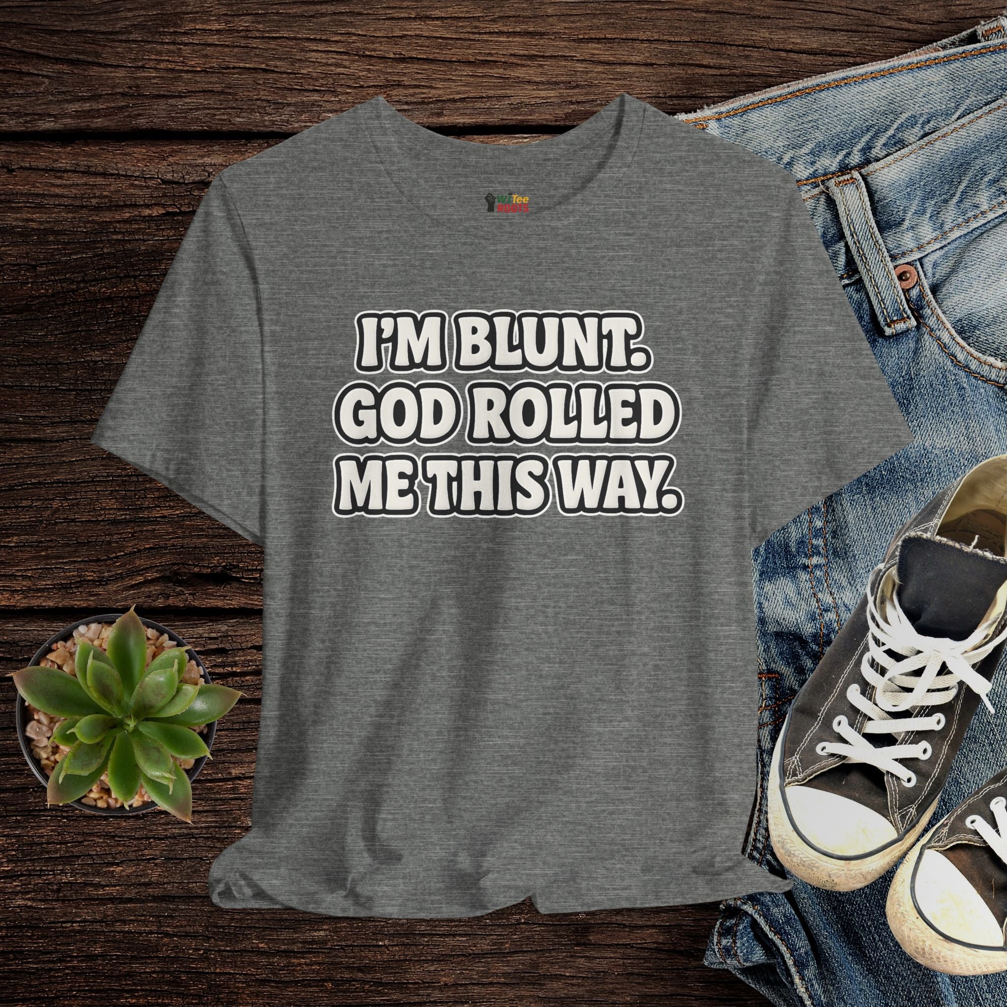 Gray t-shirt with humorous text on a wooden surface with jeans and sneakers.