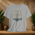 Gray t-shirt with 'WE OUT. HARRETT TUBMAN 1849' text on a wooden shelf with plants and a blurred background.