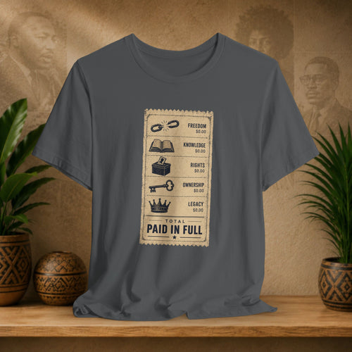 Gray t-shirt with a graphic design on a wooden surface with plants and decorative items.