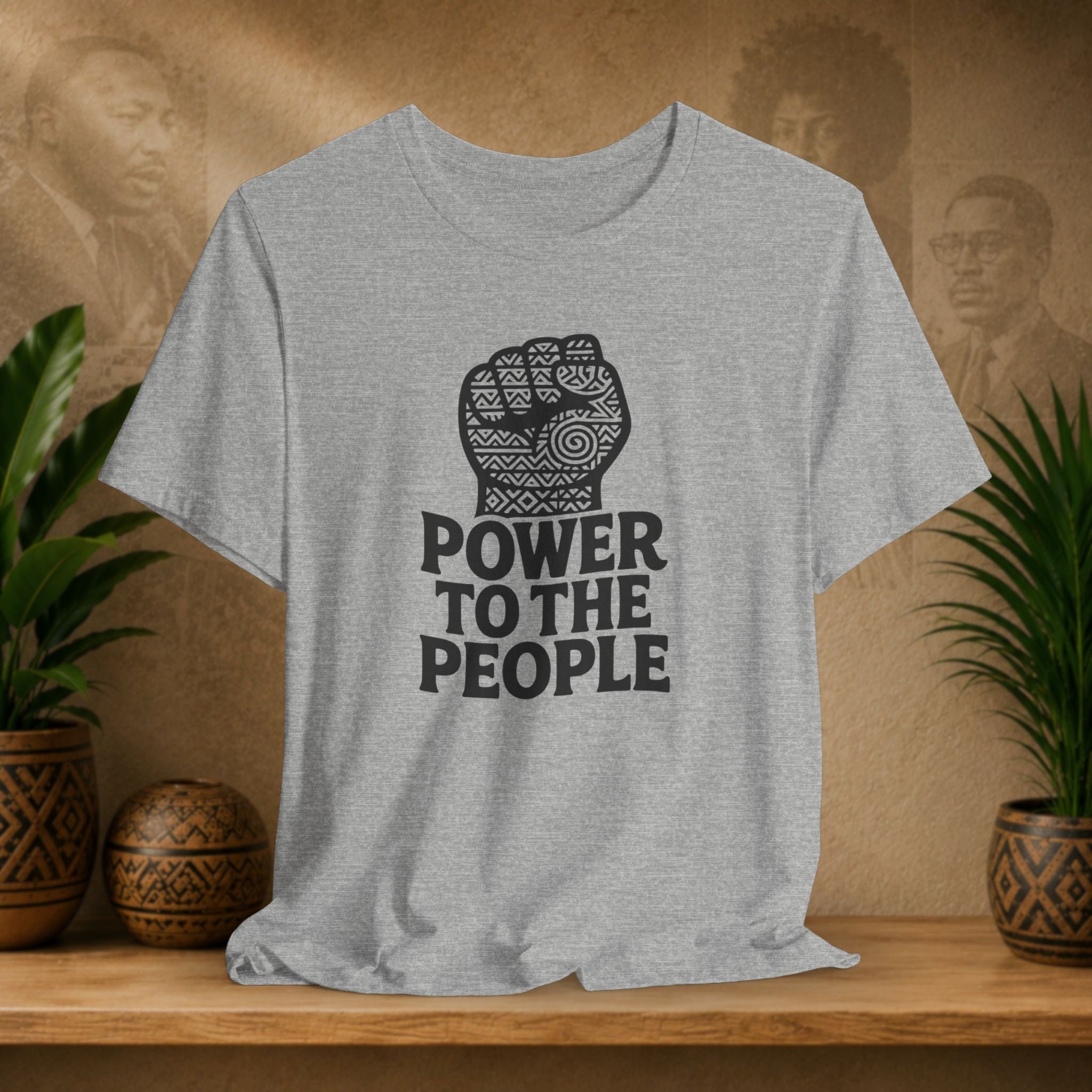 Gray t-shirt with 'Power to the People' design on a wooden surface with plants and a blurred background