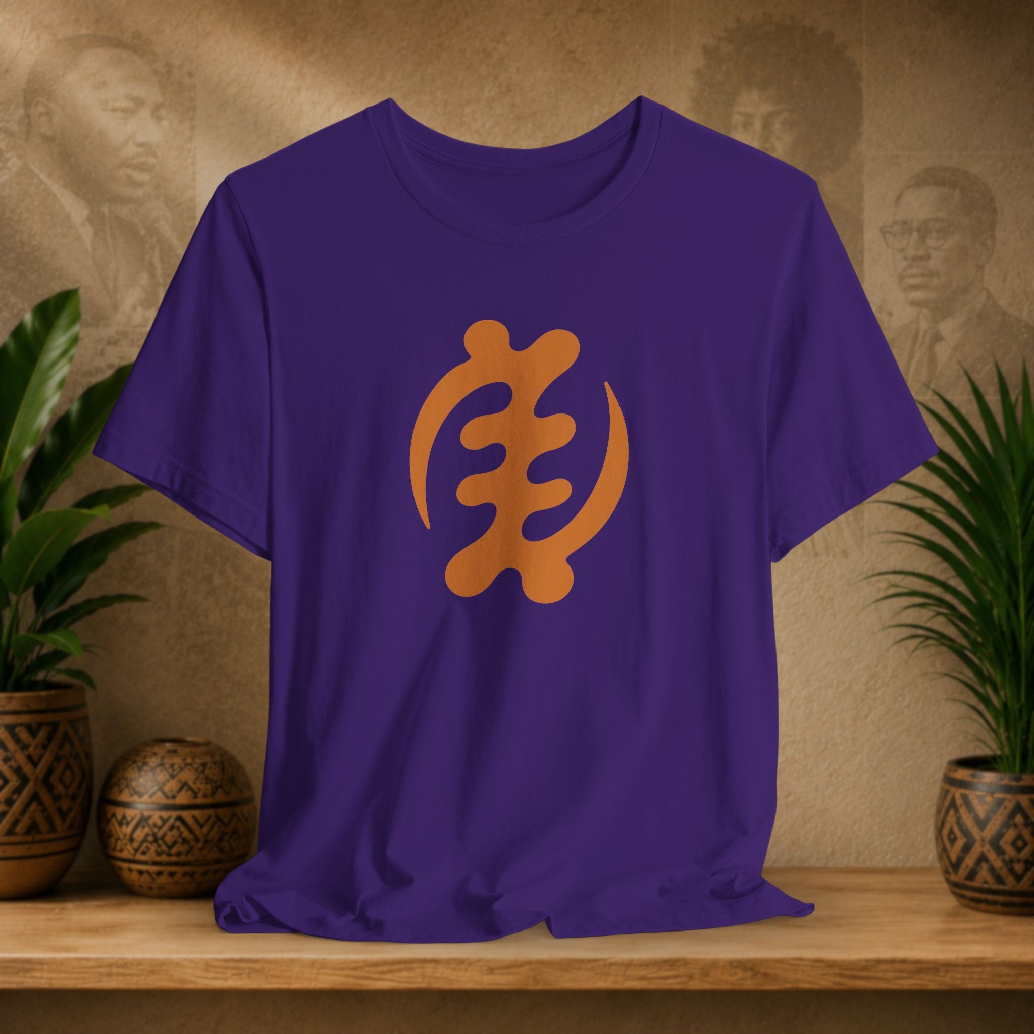 Purple t-shirt with orange symbol on a wooden surface with plants and a textured wall background