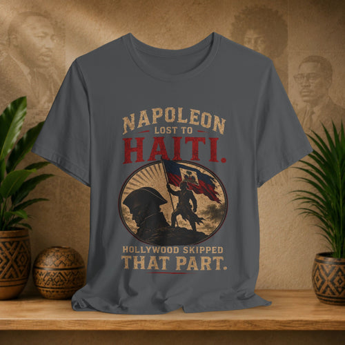 Gray t-shirt with historical graphic and text on a wooden shelf with plants and decorative items.