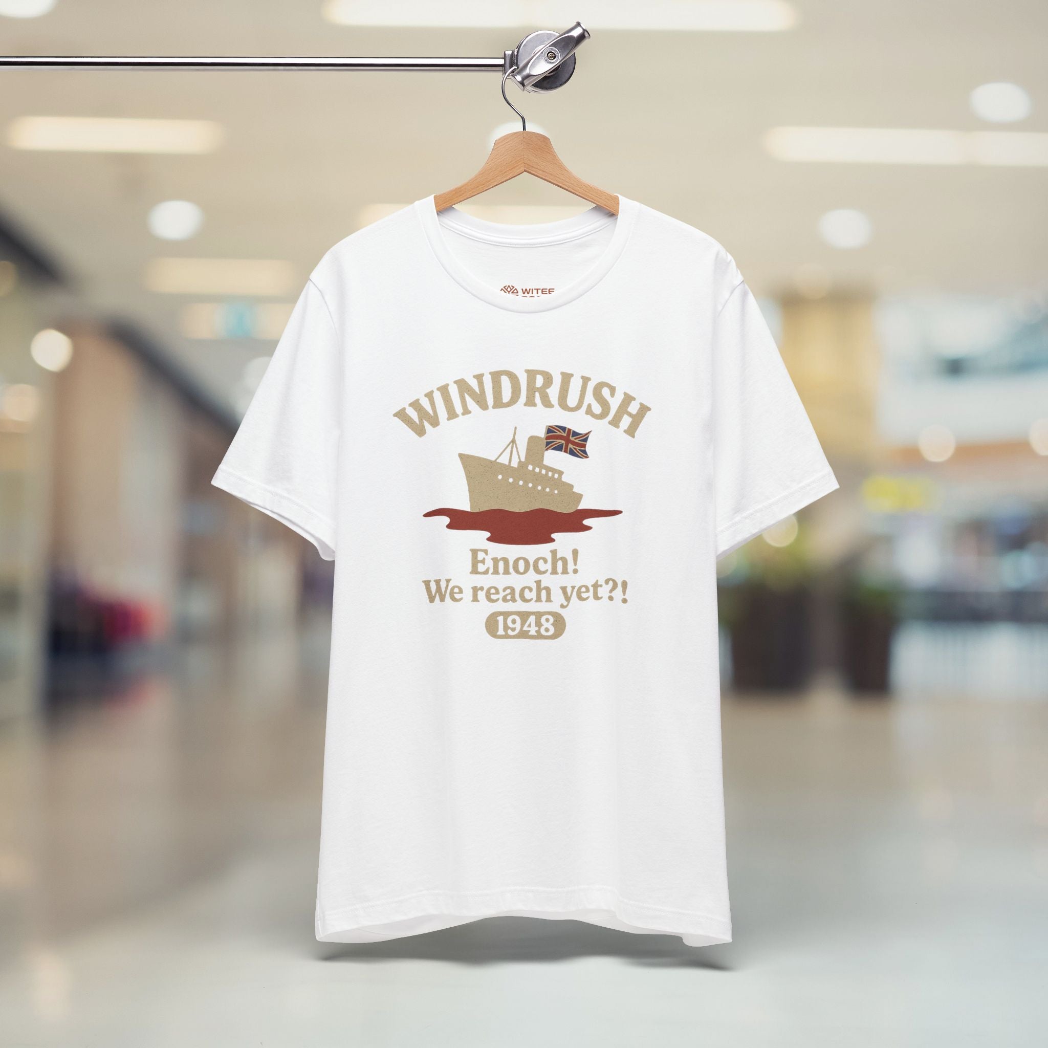 White t-shirt with 'Windrush' design on a hanger in a store.