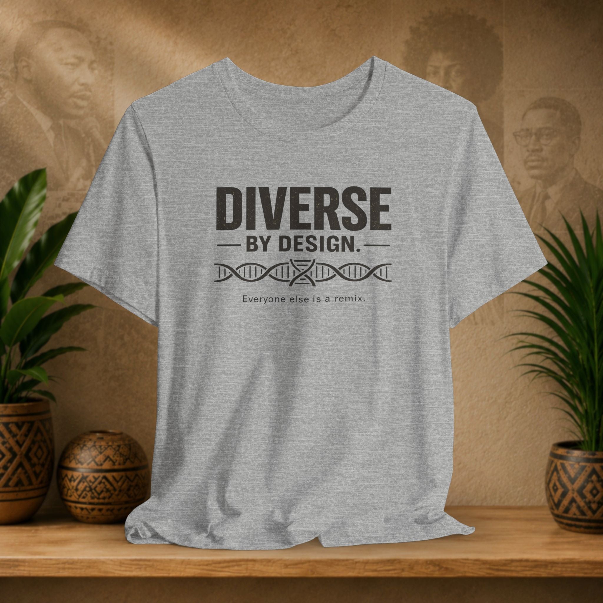 Gray t-shirt with 'Diverse by Design' text on a wooden surface with plants and a blurred background