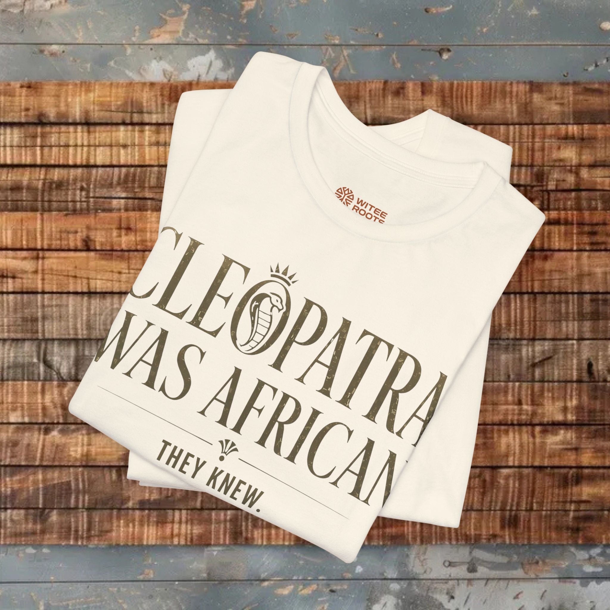 Folded t-shirt with 'Cleopatra was African, they knew' text on a wooden surface